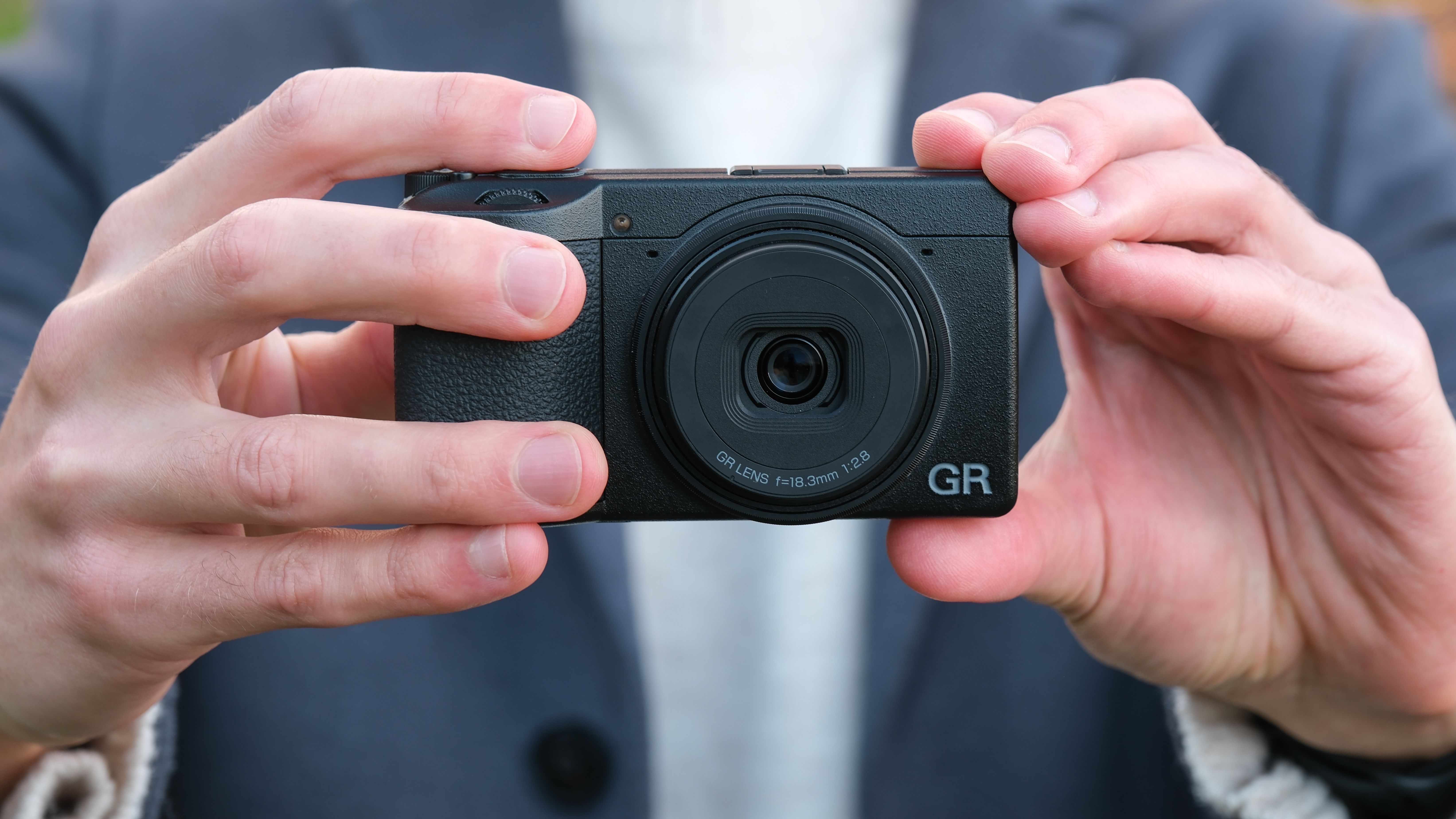 Ricoh GR IV compact camera held in a pair of hands