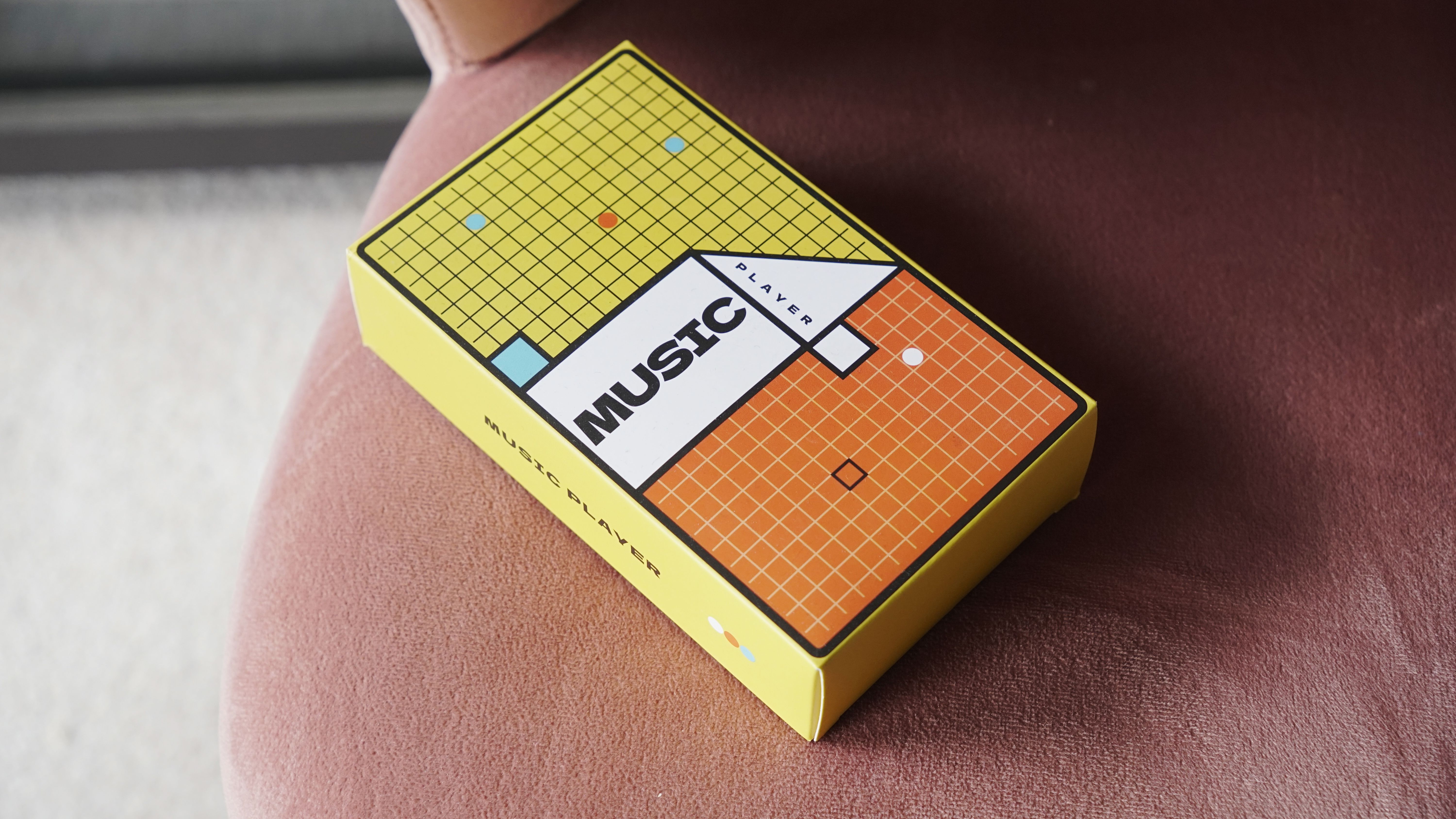 Innioasis Y1 player held in a man's hand, showing the dial and screen, with a wooden table in the background