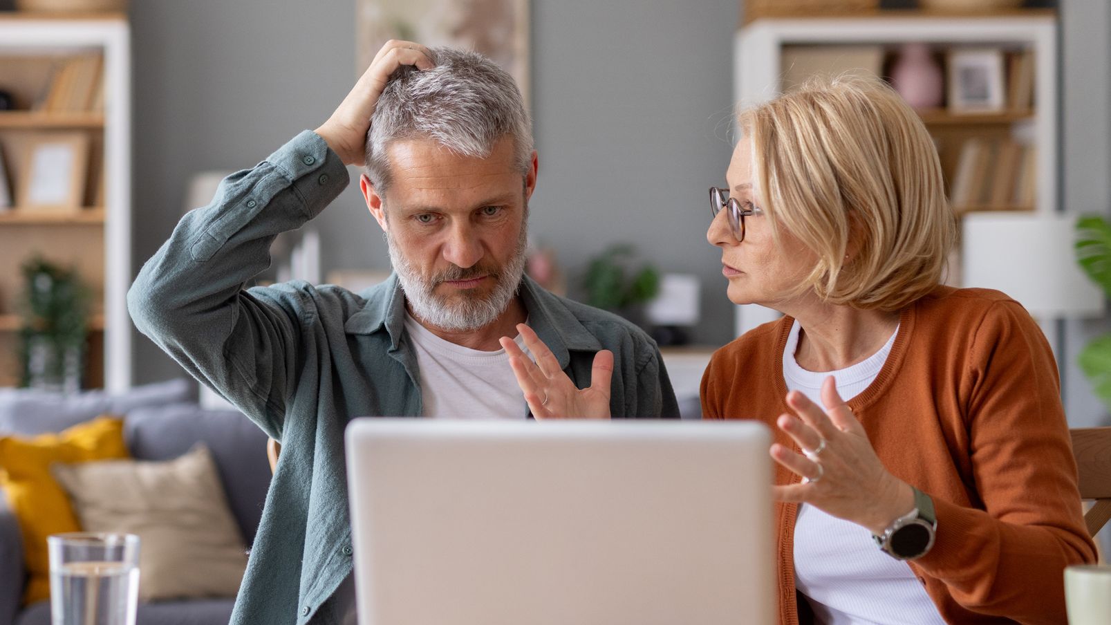 An older couple focuses on a laptop while discussing technology challenges, highlighting their relationships and problem-solving skills.