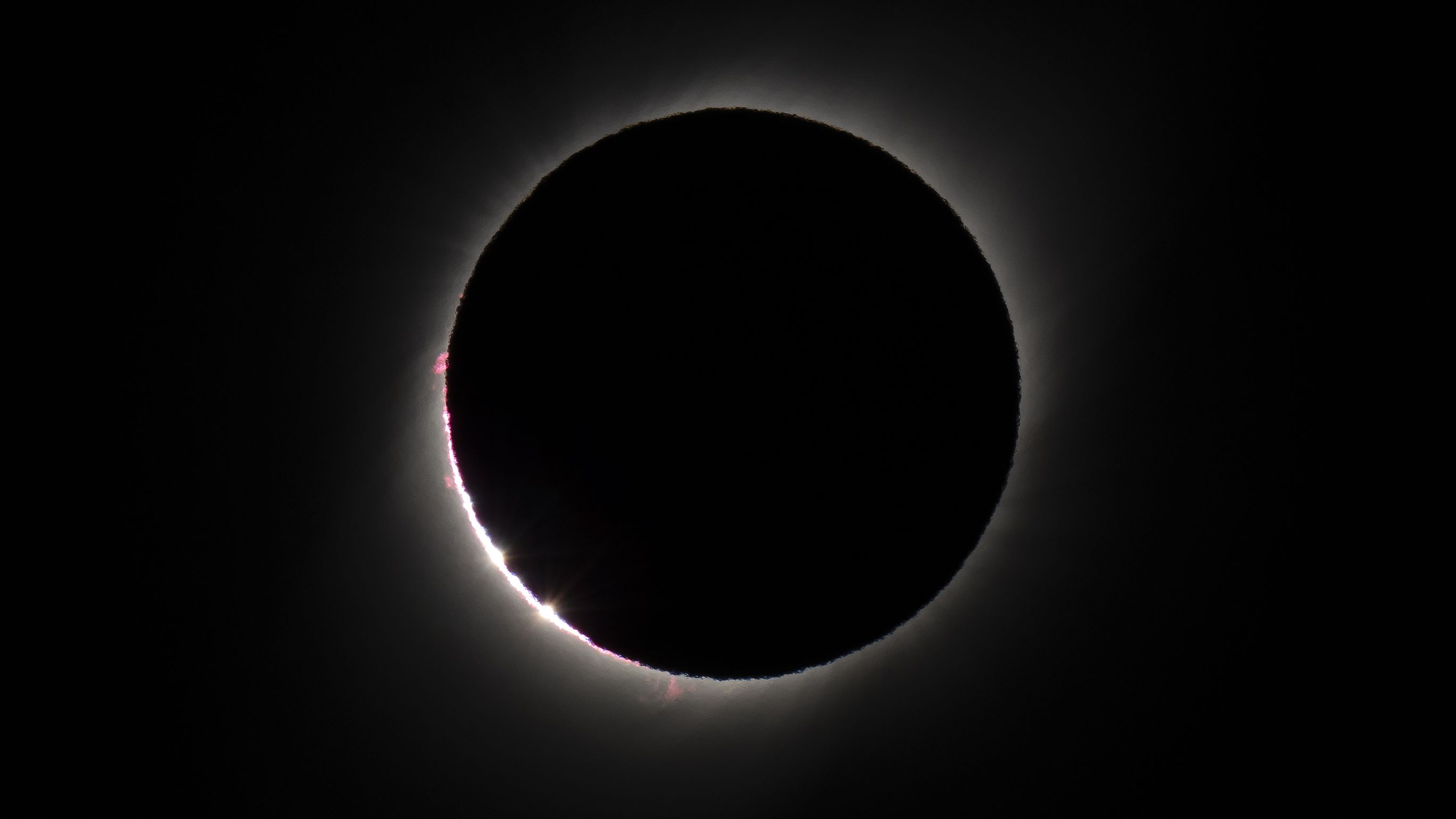 The sun's atmosphere shines from behind the moon in a black sky during a total solar eclipse.