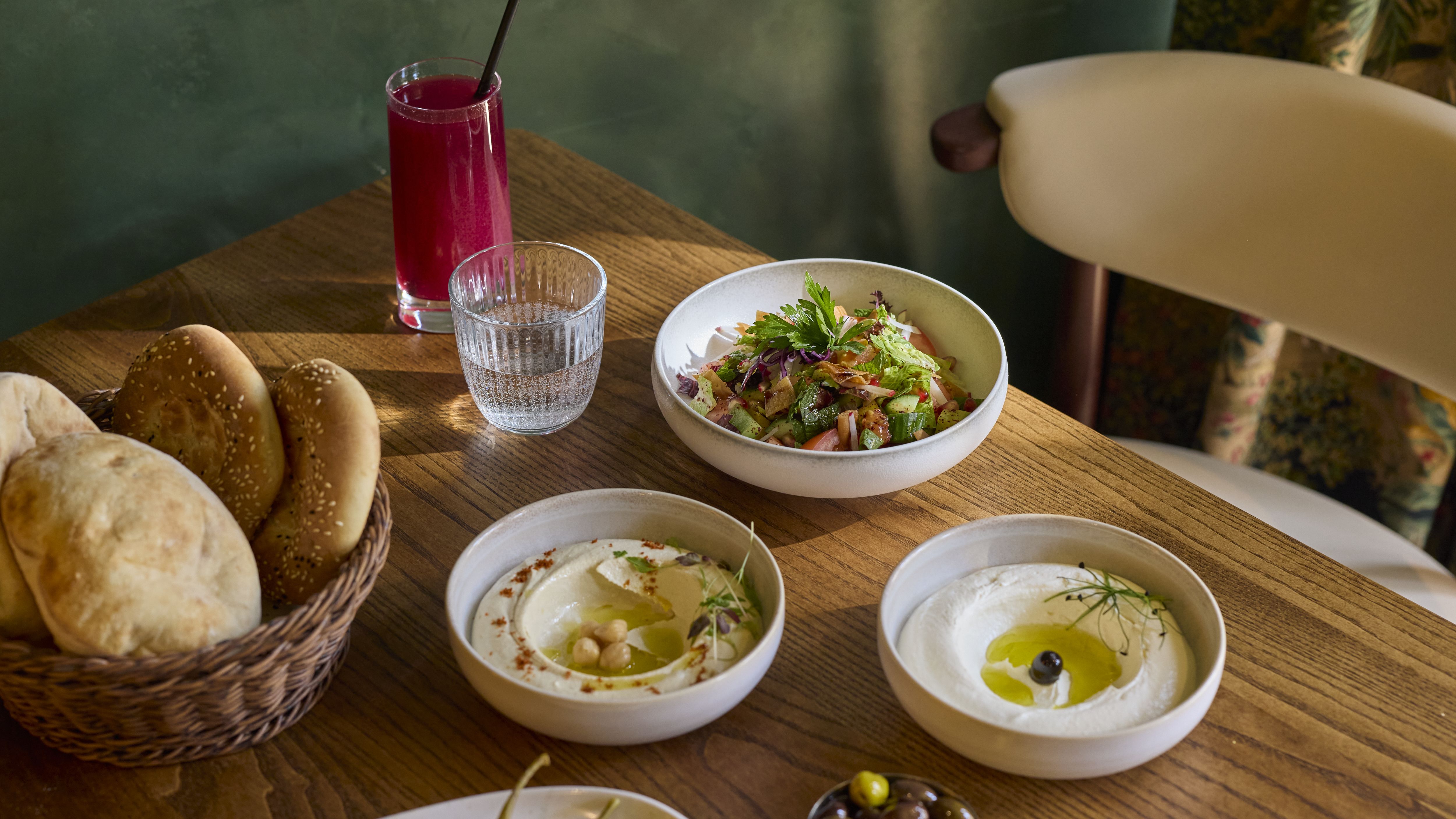 an image of four different plates of food on offer at Ishbilia on a table at the restaurant, with a basket of bread, olives, and a tall soft drink