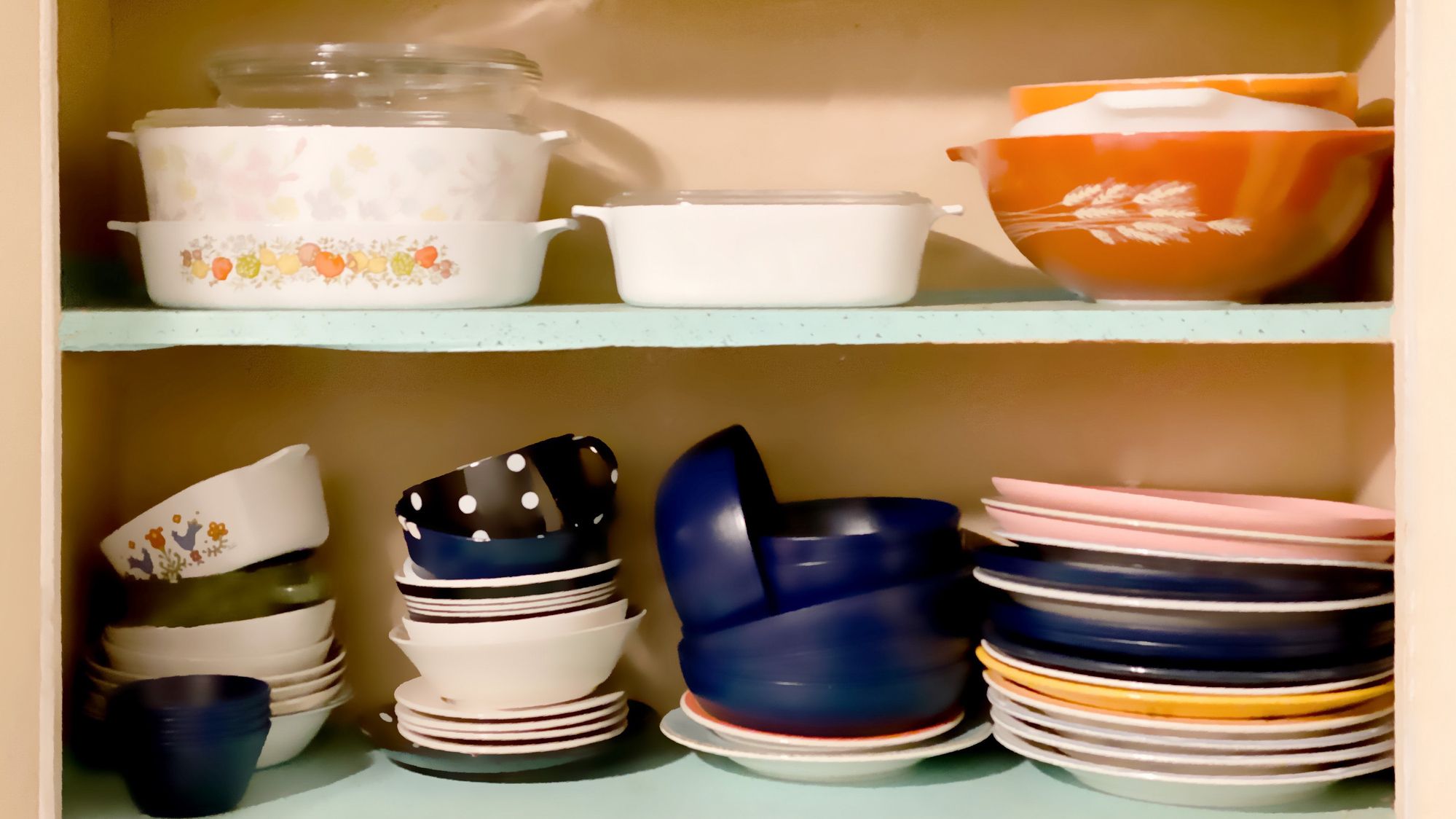 Vintage 1950s white wall kitchen cabinets open revealing shelves of old-fashioned kitchenware