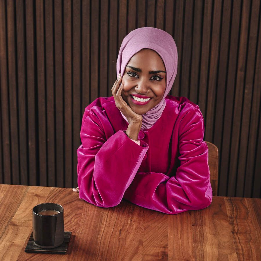 Nadiya Hussain sitting at a wooden table and smiling at the camera
