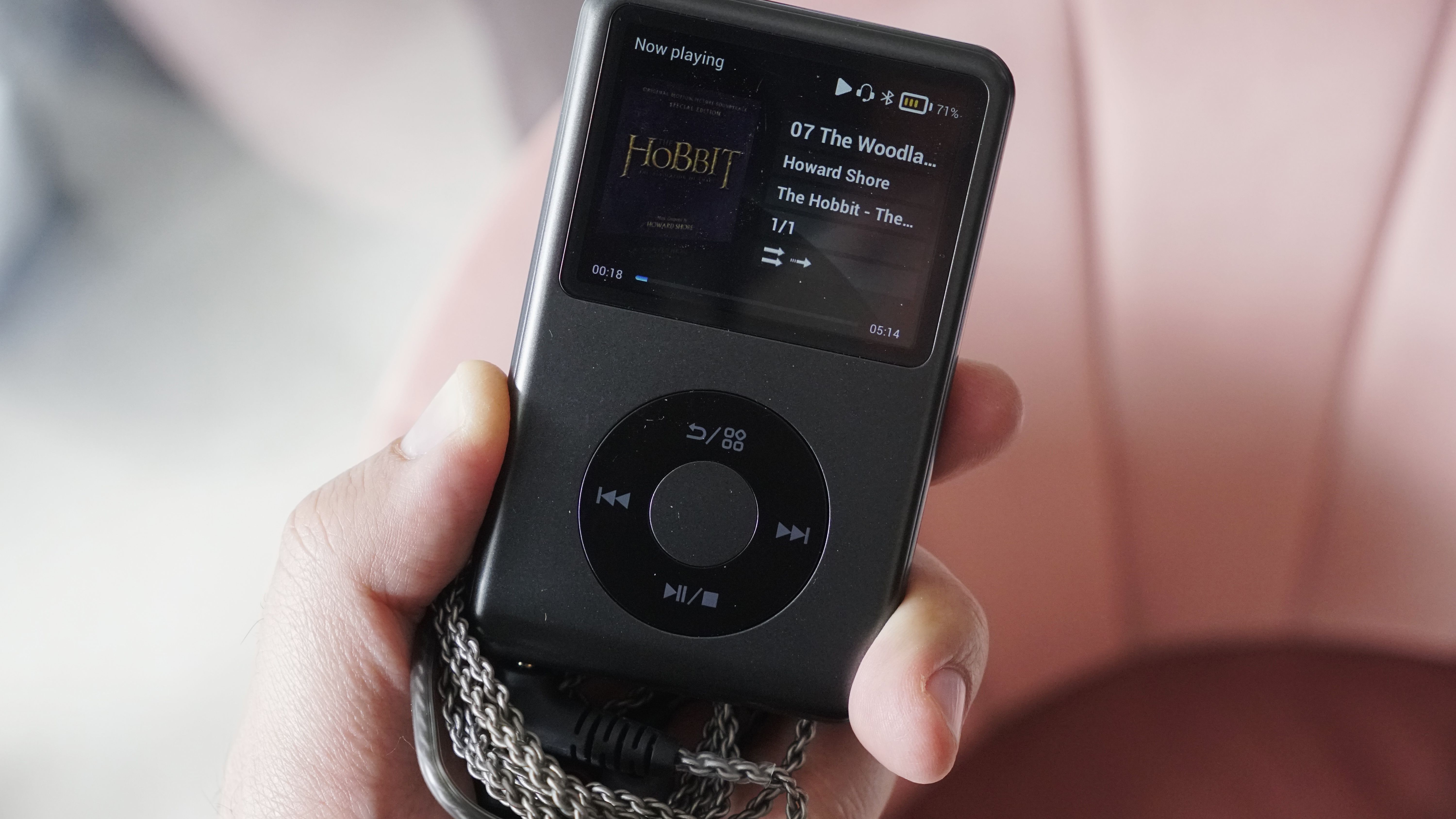 Innioasis Y1 player held in a man's hand, showing the dial and screen, with a wooden table in the background