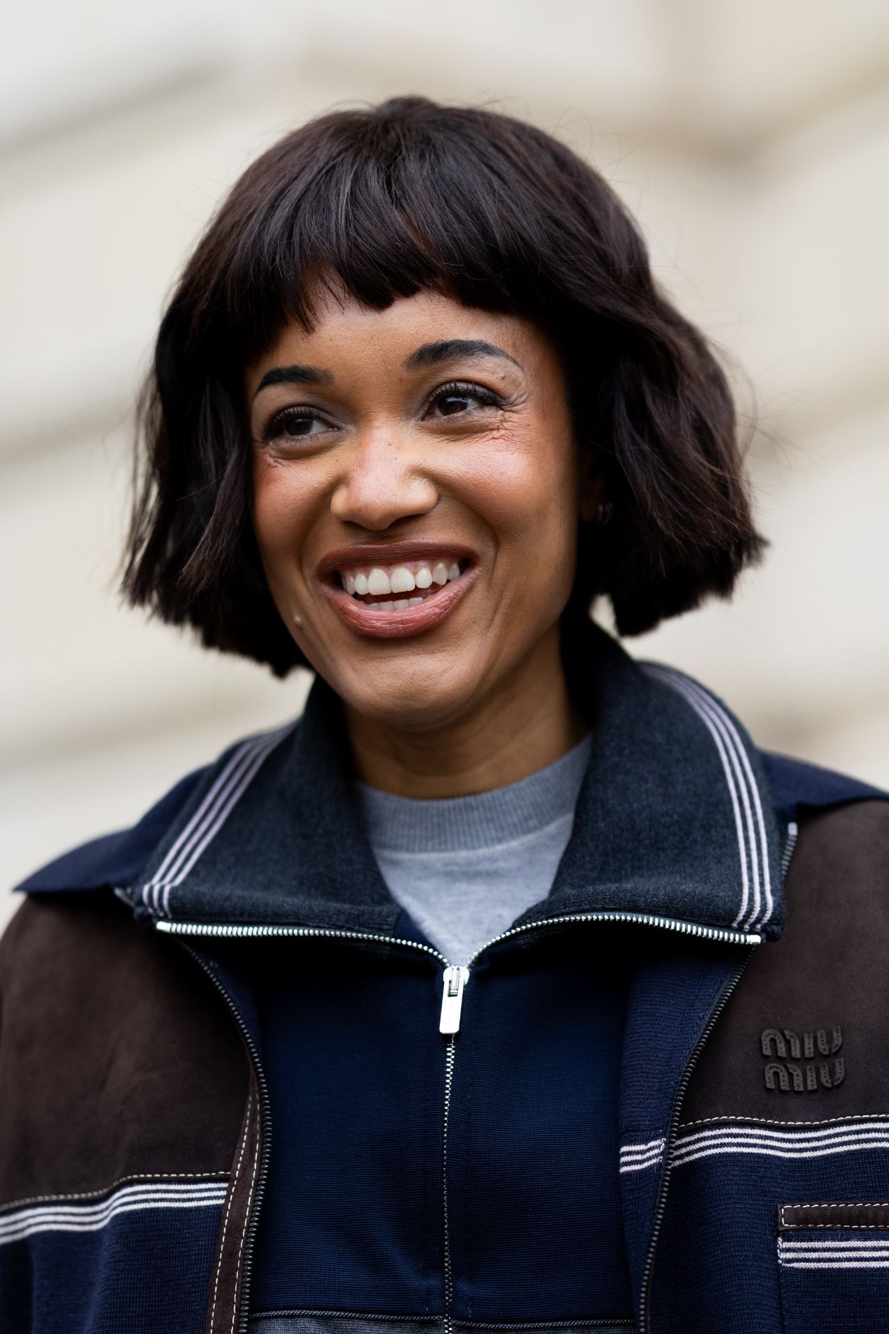 Tamu Mcpherson wears a navy and chocolate brown color-blocked zip-up jacket with contrast topstitching over a grey crewneck and navy layers finished with a short choppy bob