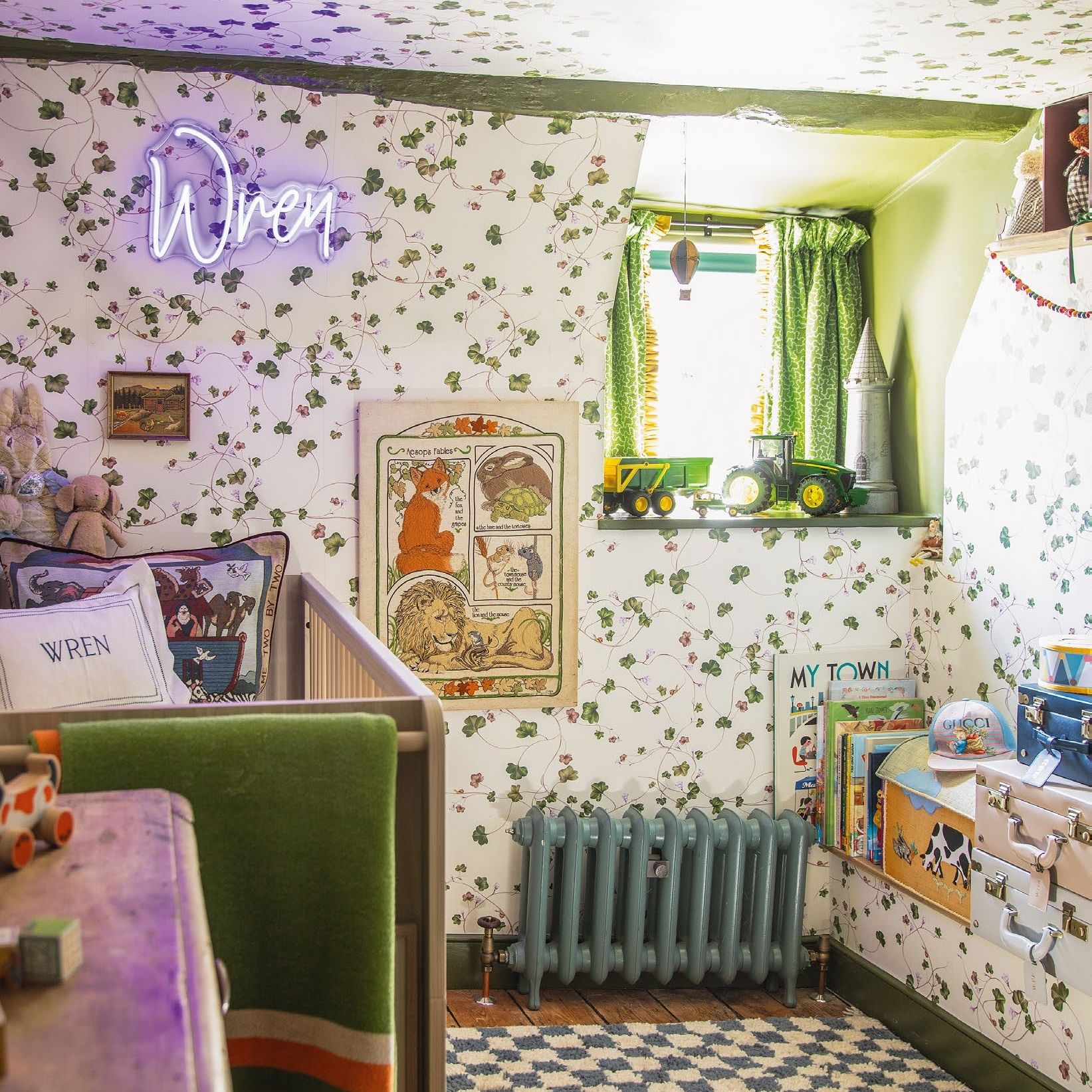 Child&#039;s bedroom with ivy patterned wallpaper on walls and ceiling. With neon name sign, painted radiator, chequered rug and wooden crib.