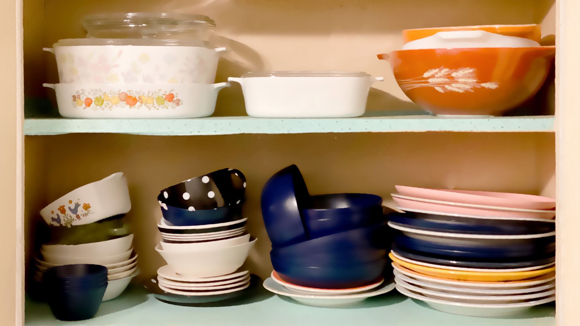 Vintage 1950s white wall kitchen cabinets open revealing shelves of old-fashioned kitchenware