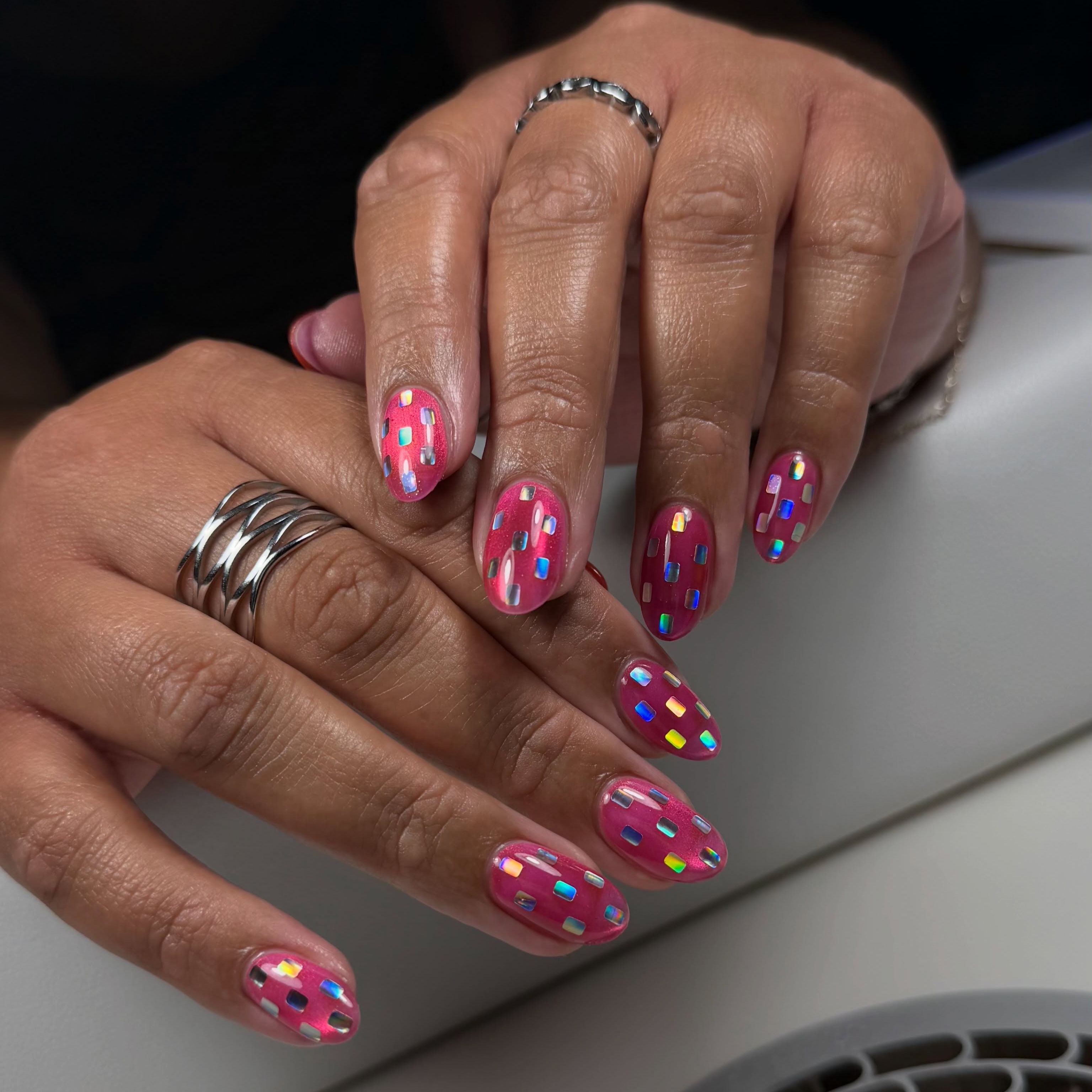Bright pink oval nails covered in small multicolored metallic paillettes
