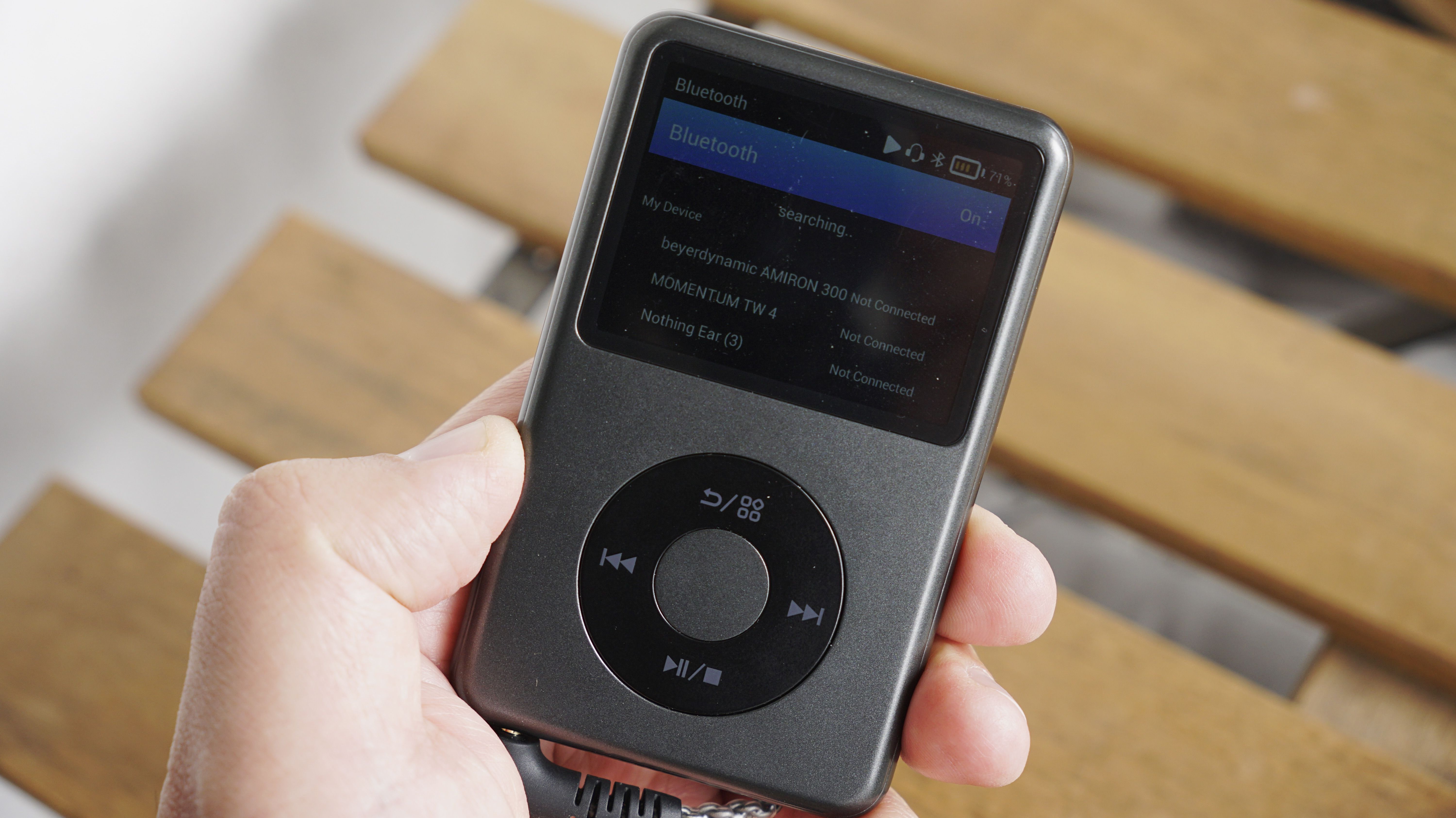 Innioasis Y1 player held in a man's hand, showing the dial and screen, with a wooden table in the background