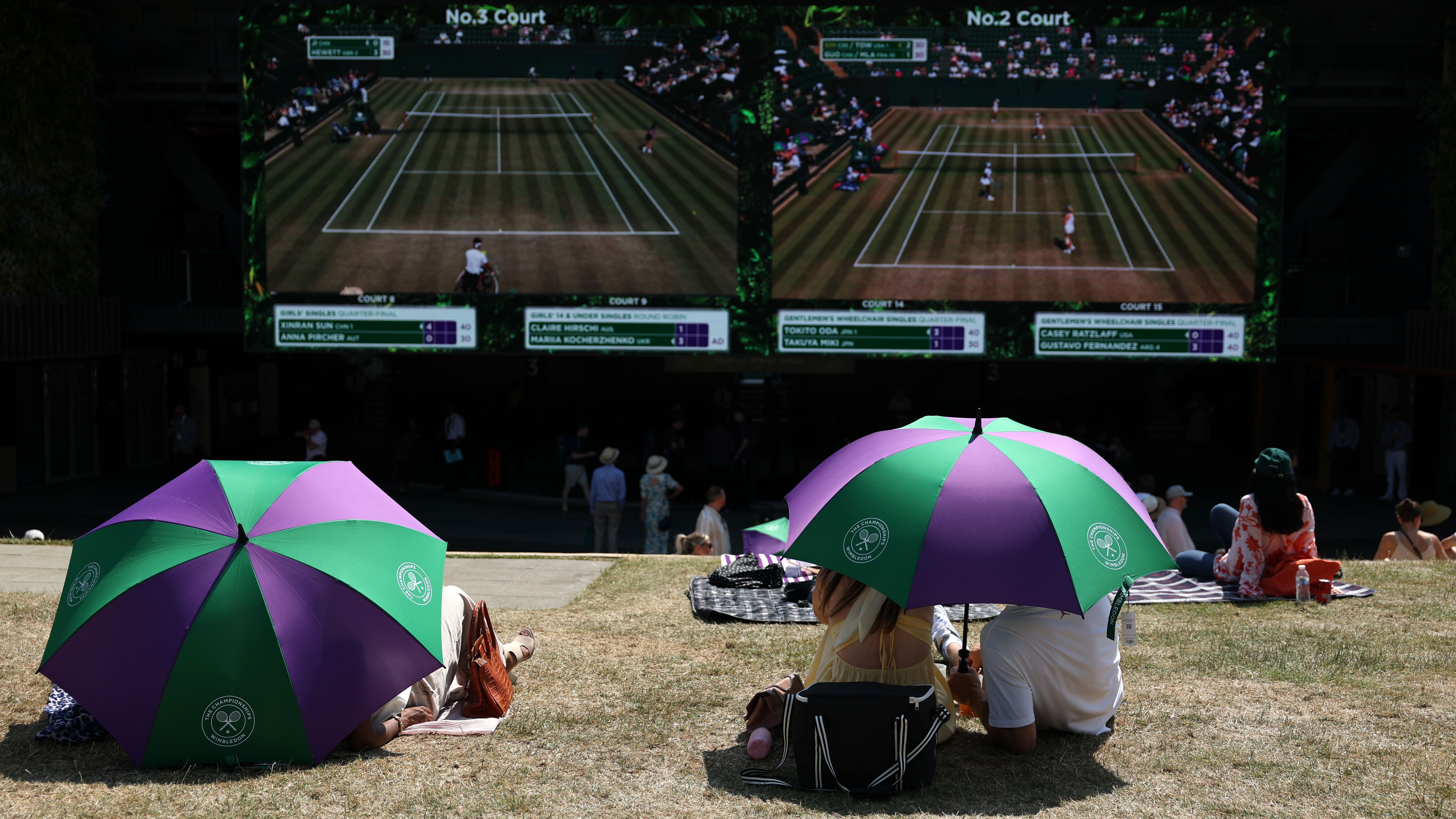 Two couples under parasols watch the screens at Wimbledon