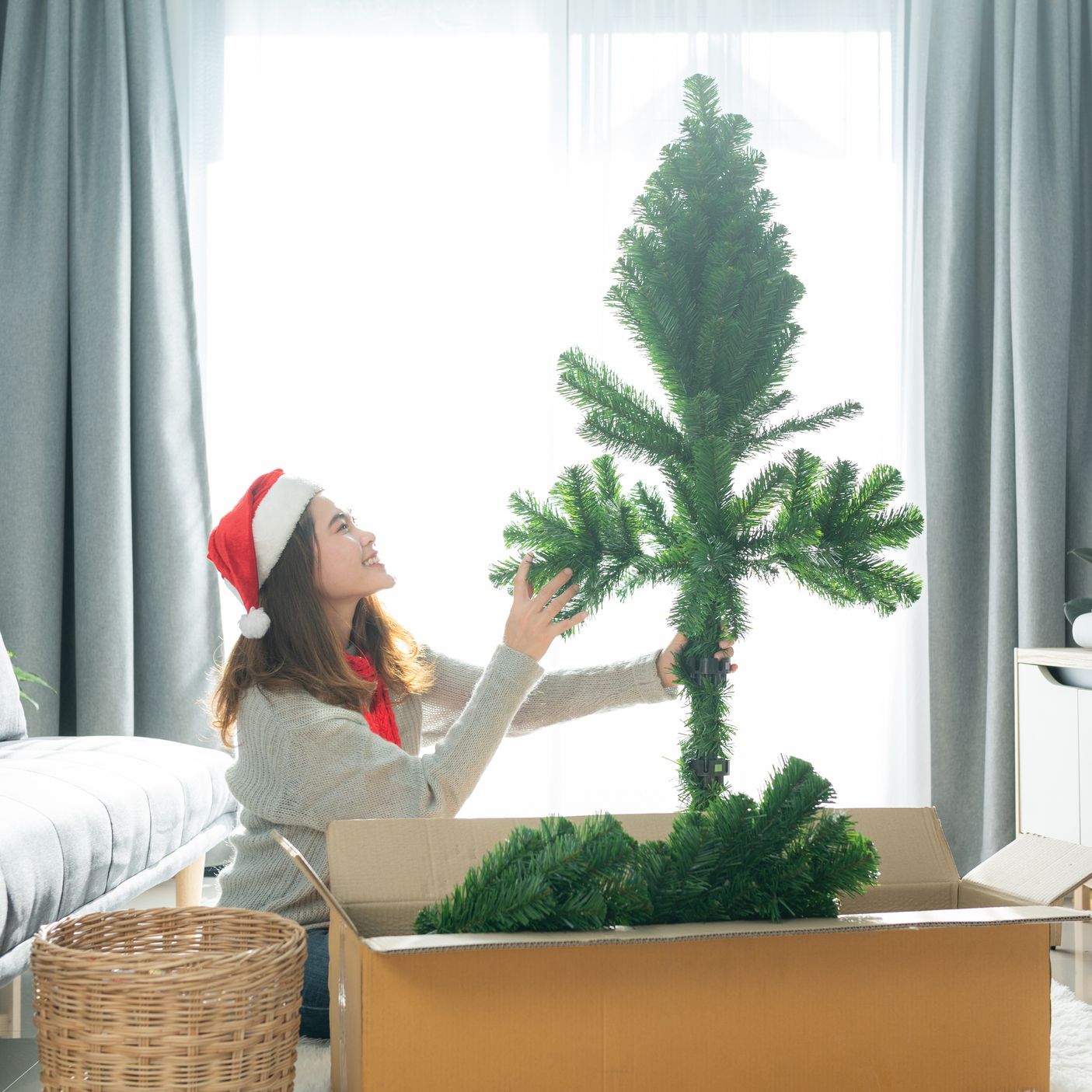 A woman assembles an artificial Christmas tree from a box in her living room.