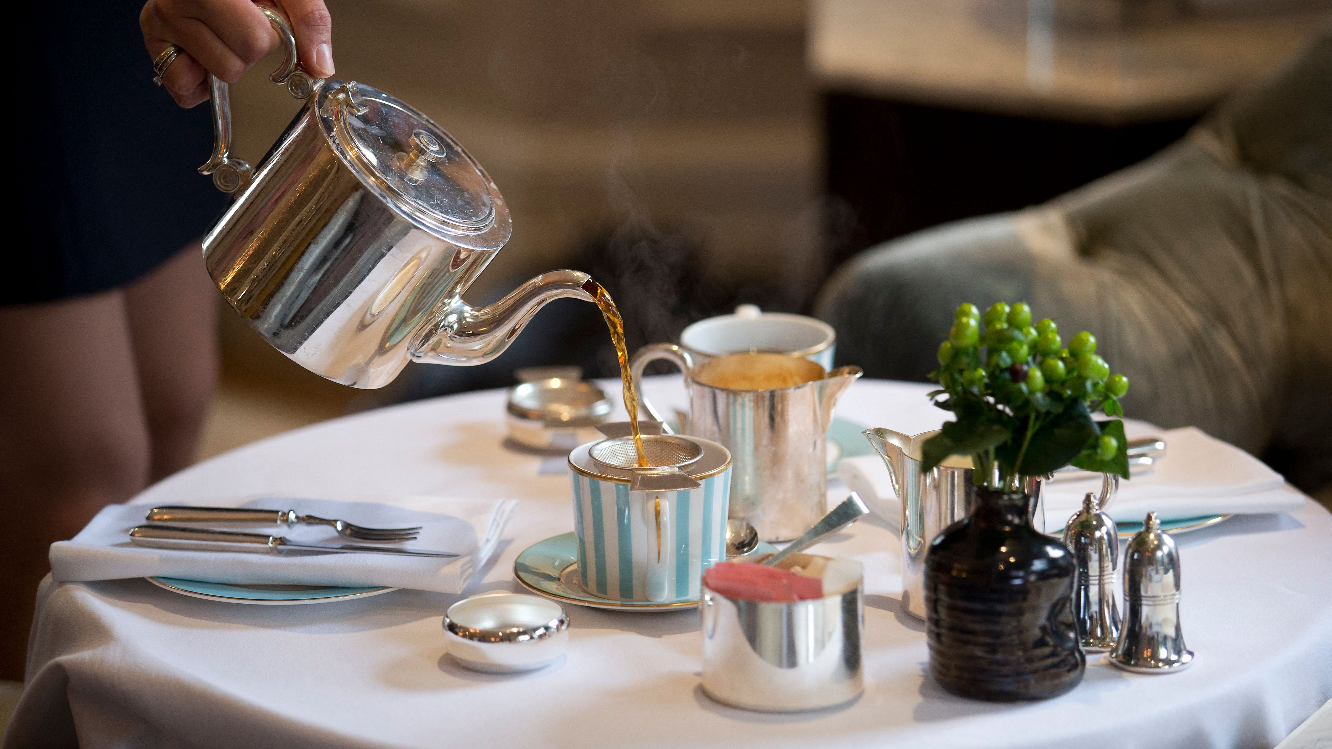 A member of hotel staff pours a woman a cup of tea at the Kensington Hotel in London on August 11, 2016. The popularity of afternoon tea has London hotels vying to attract a new wave of customers by inventing twists on the classic English indulgence -- although with tapas and takeaways on offer, some say the trend is going too far. (Photo by JUSTIN TALLIS / AFP) / TO GO WITH AFP STORY BY ROBIN MILLARD (Photo by JUSTIN TALLIS/AFP via Getty Images)
