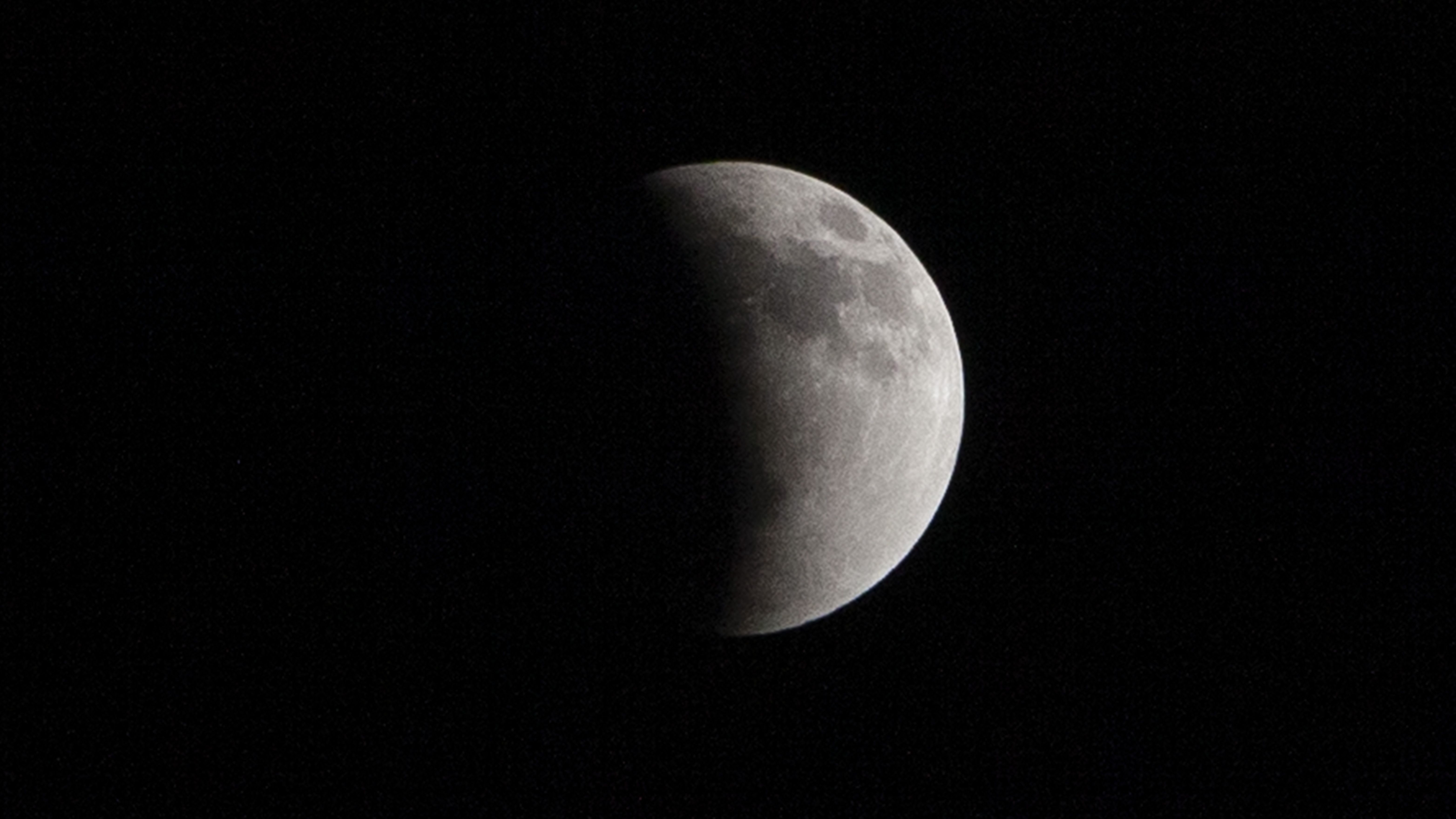 Uma lua cheia é fotografada em um céu negro com sua metade esquerda banhada pela sombra curva da Terra durante um eclipse lunar.