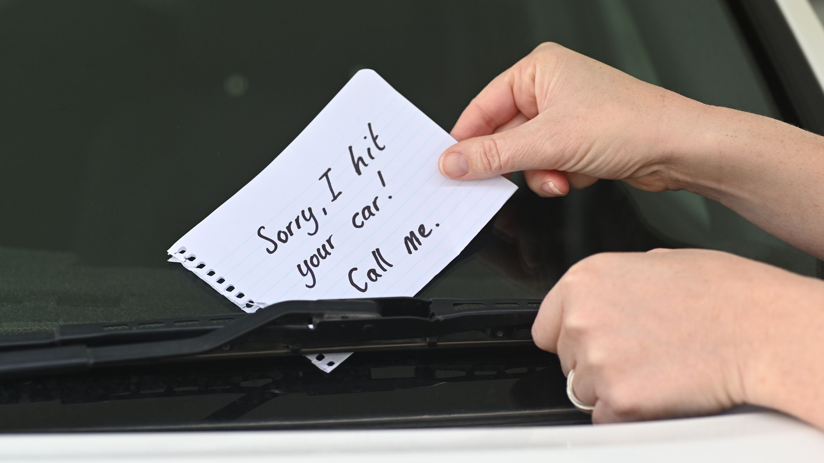 A person leaving a note on a car after they've hit it.