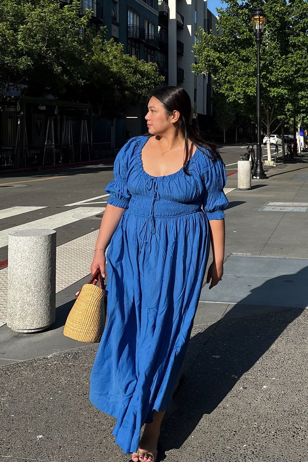 Woman wears blue dress, carries basket bag and wears sandals