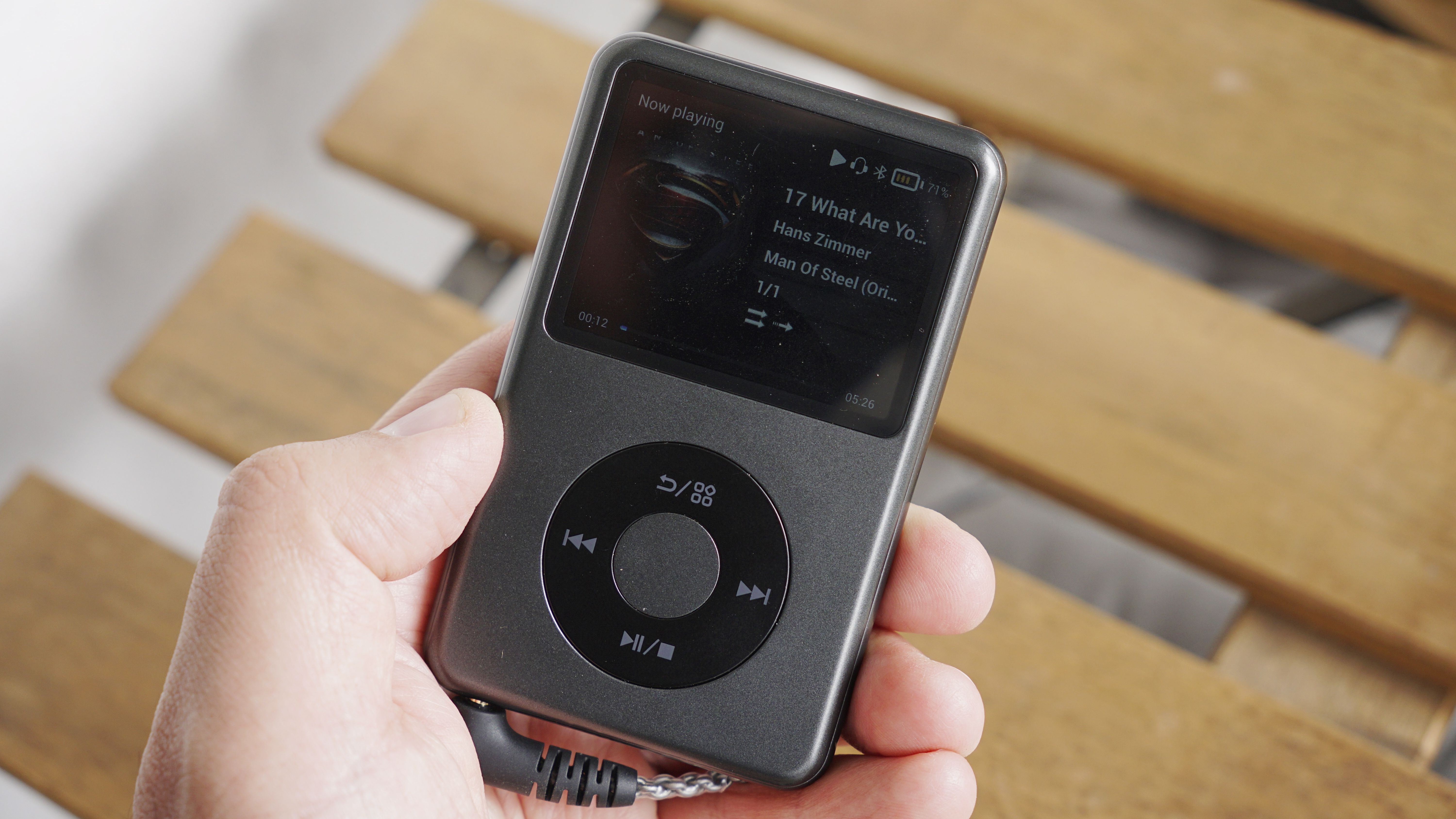 Innioasis Y1 player held in a man's hand, showing the dial and screen, with a wooden table in the background
