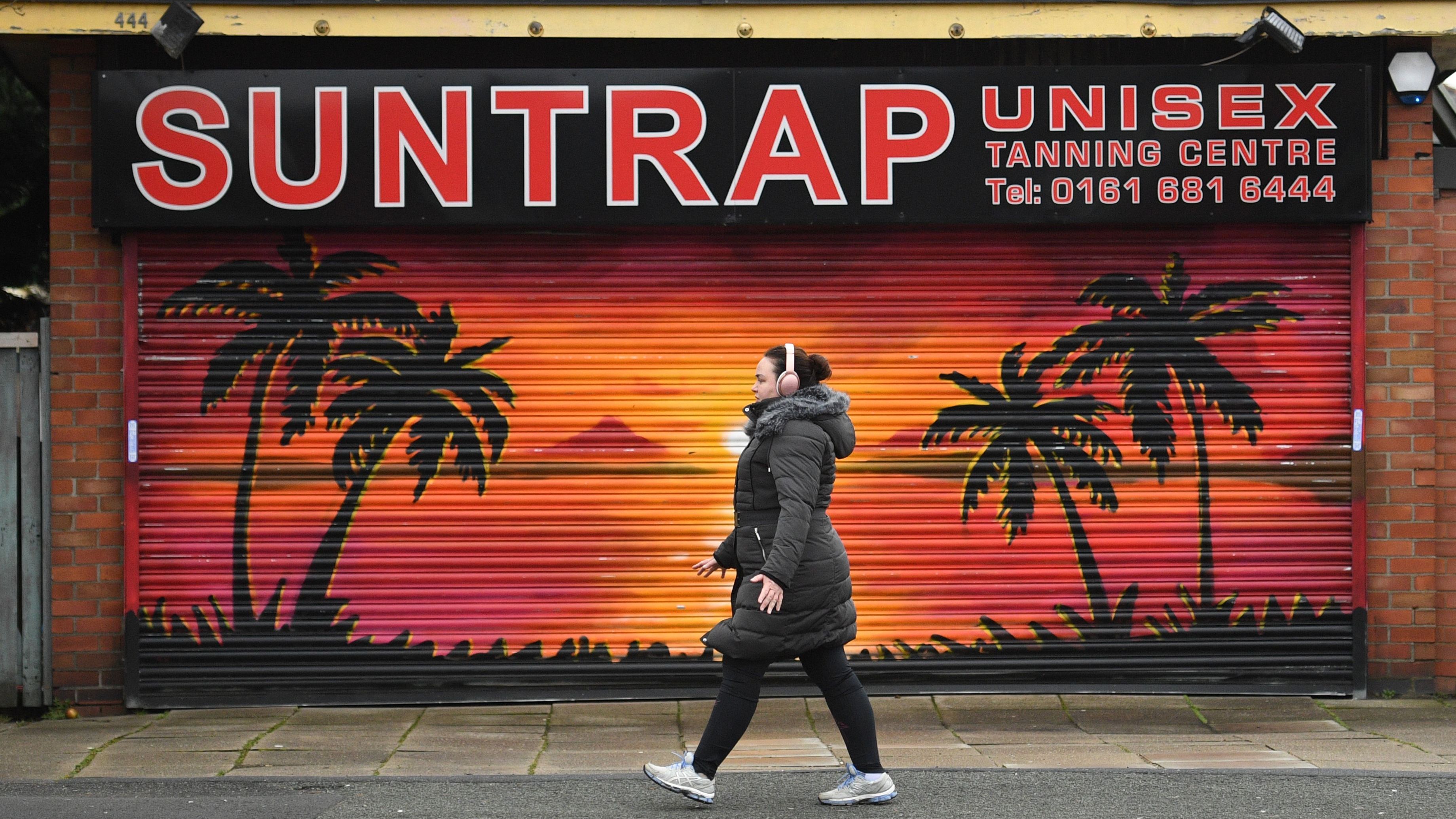 A woman walks past an advertisment for a tanning salon in Manchester on February 19, 2021. (Photo by Oli SCARFF / AFP) (Photo by OLI SCARFF/AFP via Getty Images)