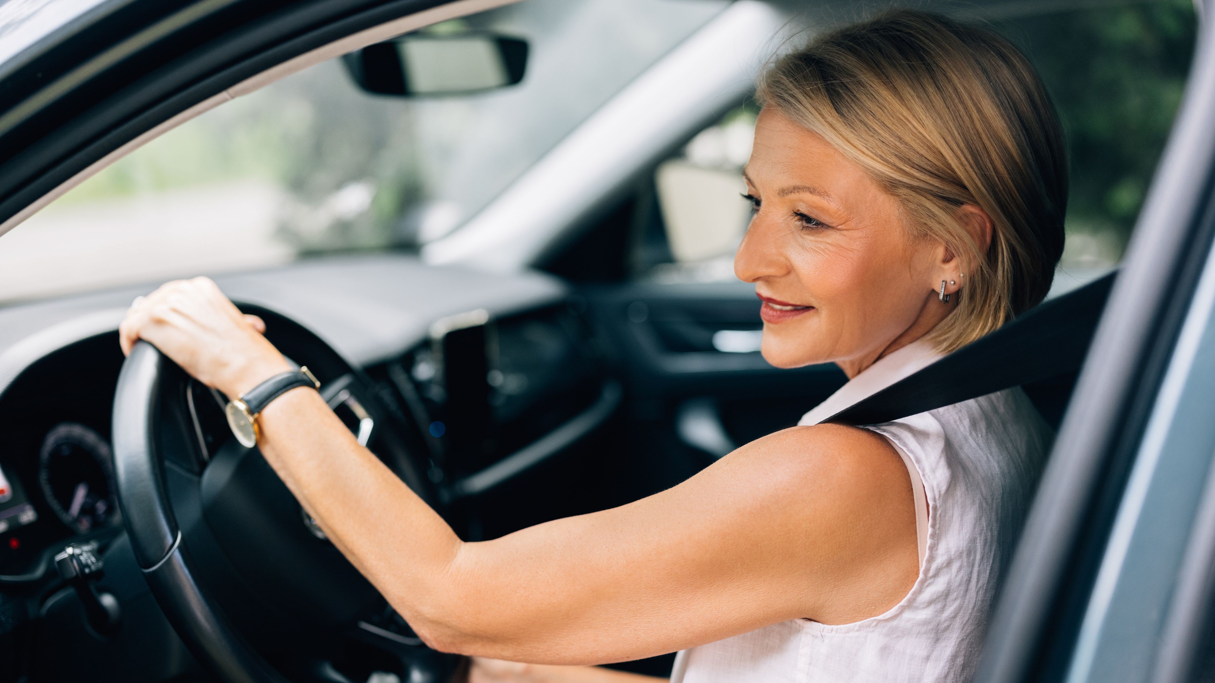 A mature businesswoman checks her mirror while driving her car.