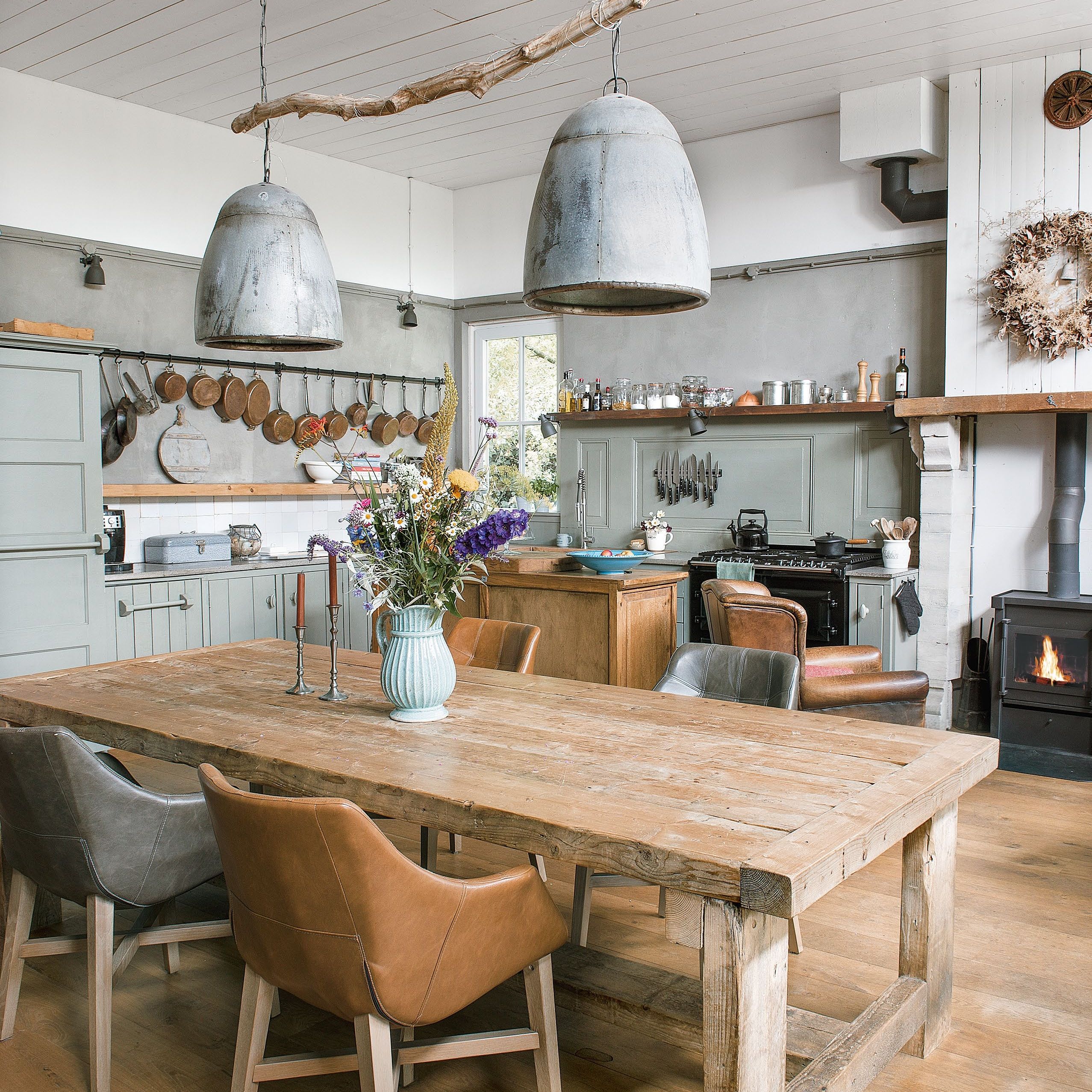 open-plan kitchen diner with large industrial style pendant lights over wooden table and sage green kitchen units