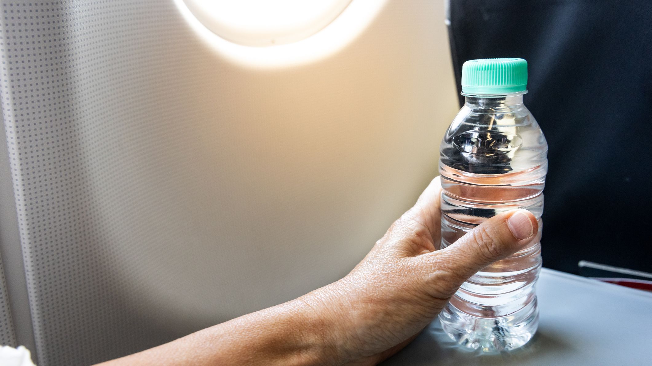 A hand holding a bottle of water on an airplane tray table