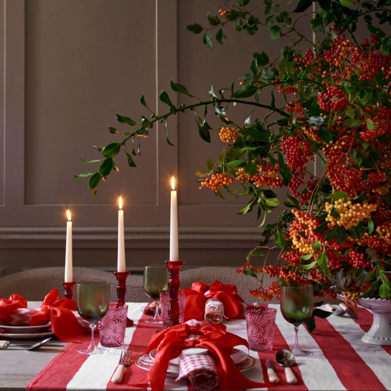 Fall tablescape with red and white striped tablecloth, seasonal berries, red candlestick holders and taper candles