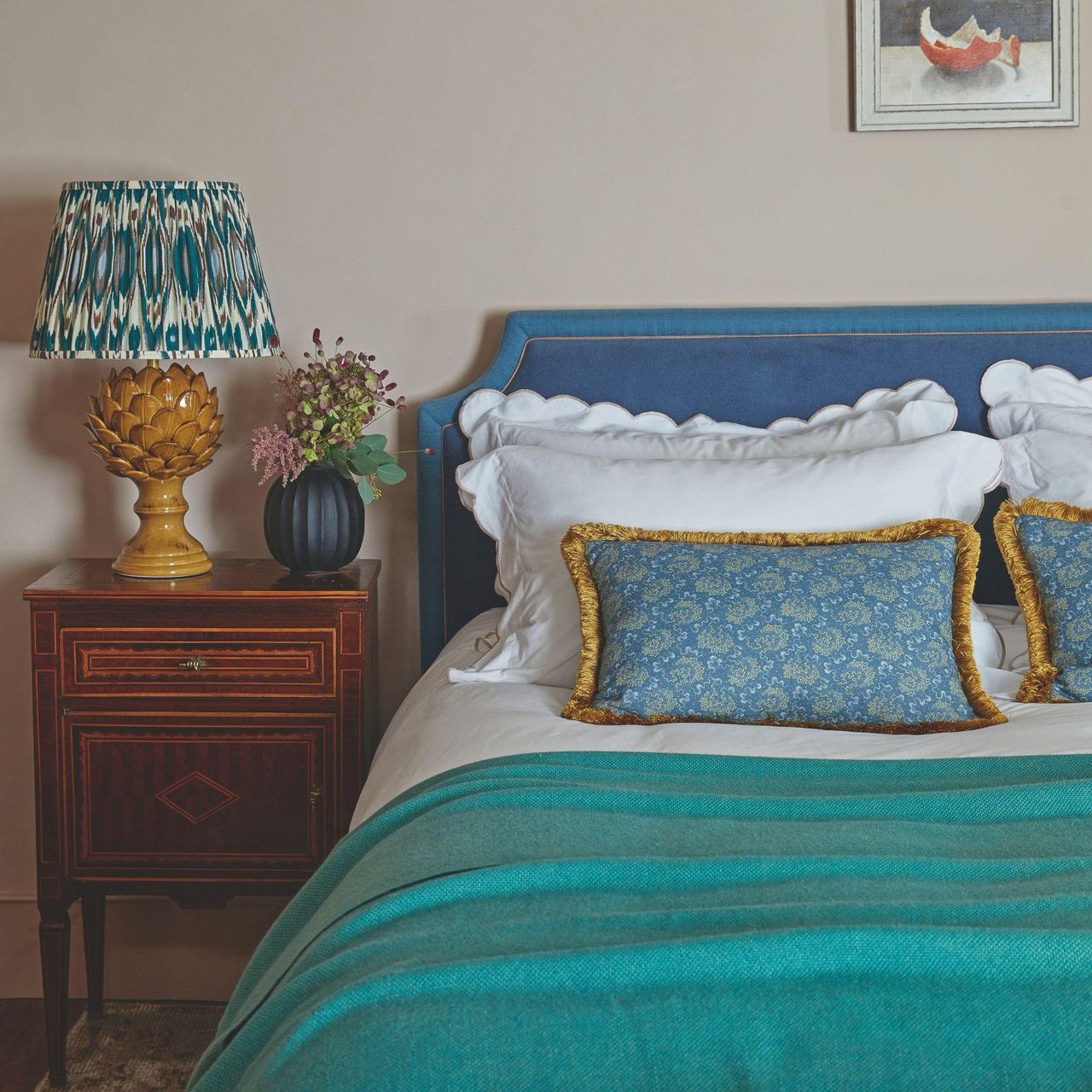 Bedroom with warm beige walls and bed with blue headboard and turquoise throw with a wooden bedside table