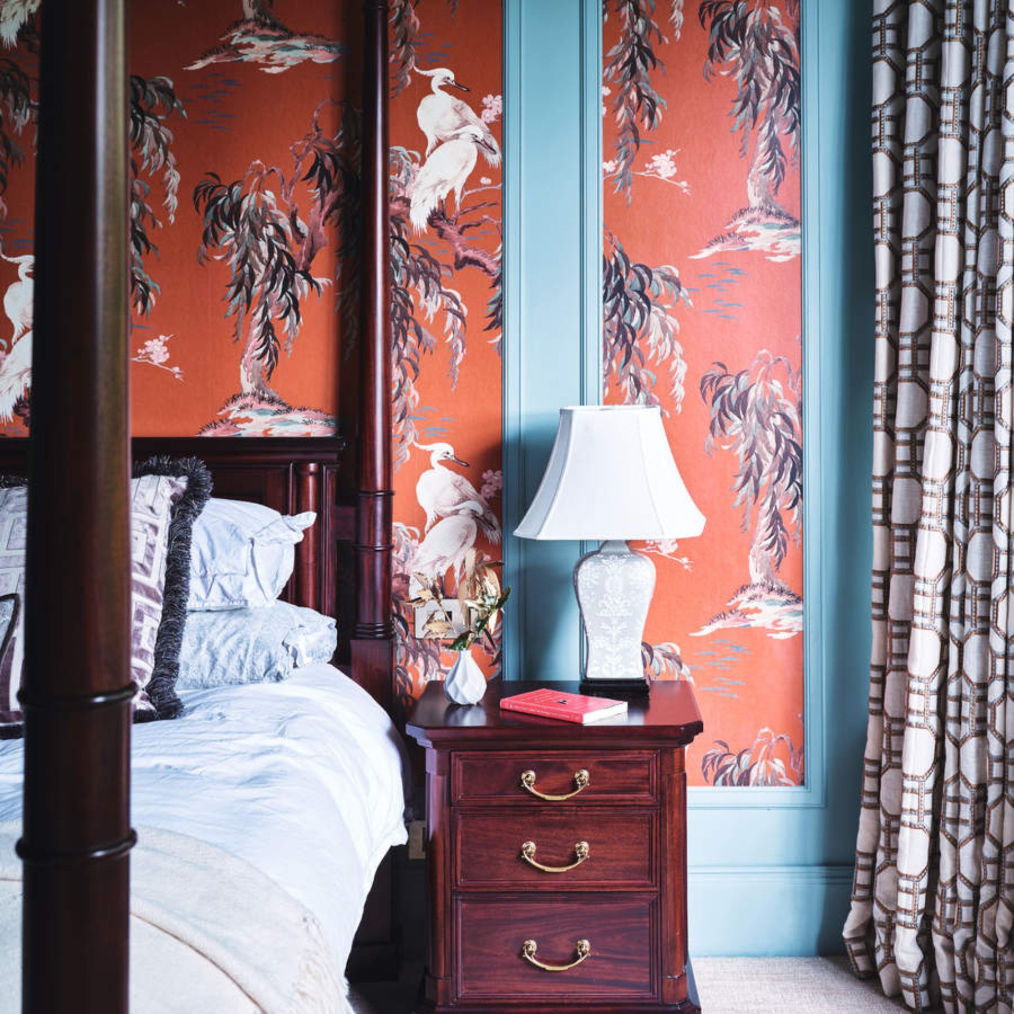 Blue pillows on a dark wood four poster against blue walls with orange patterned wallpaper. 
