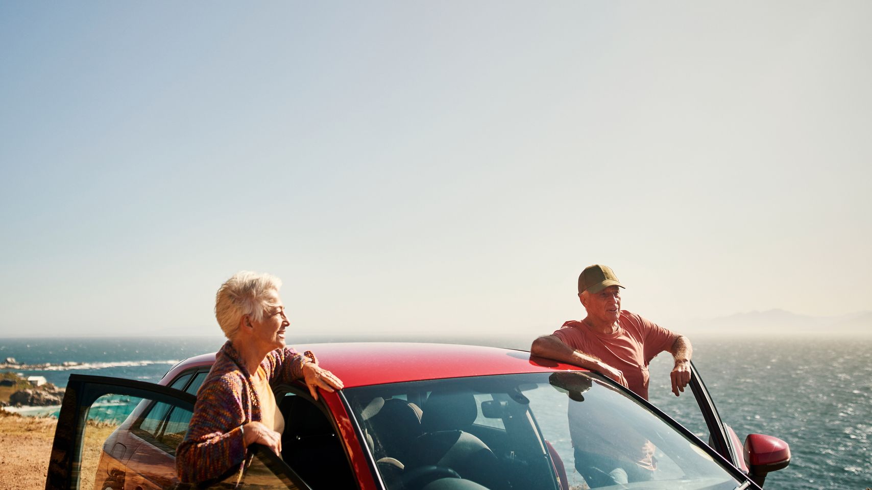 A senior couple standing beside car at a scenic outlook.
