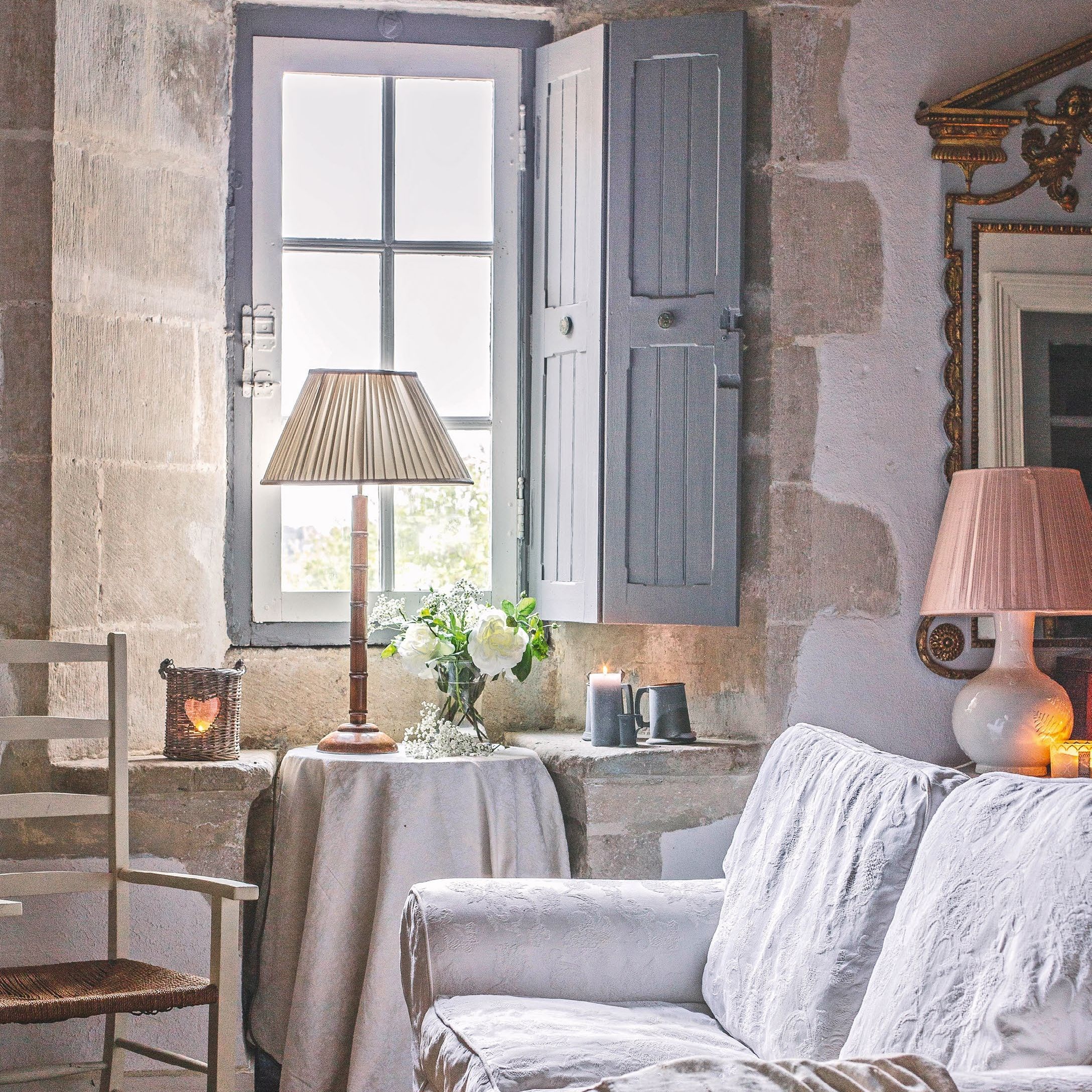 view of a living room in a rustic french property with pale blue window shutters and stone walls