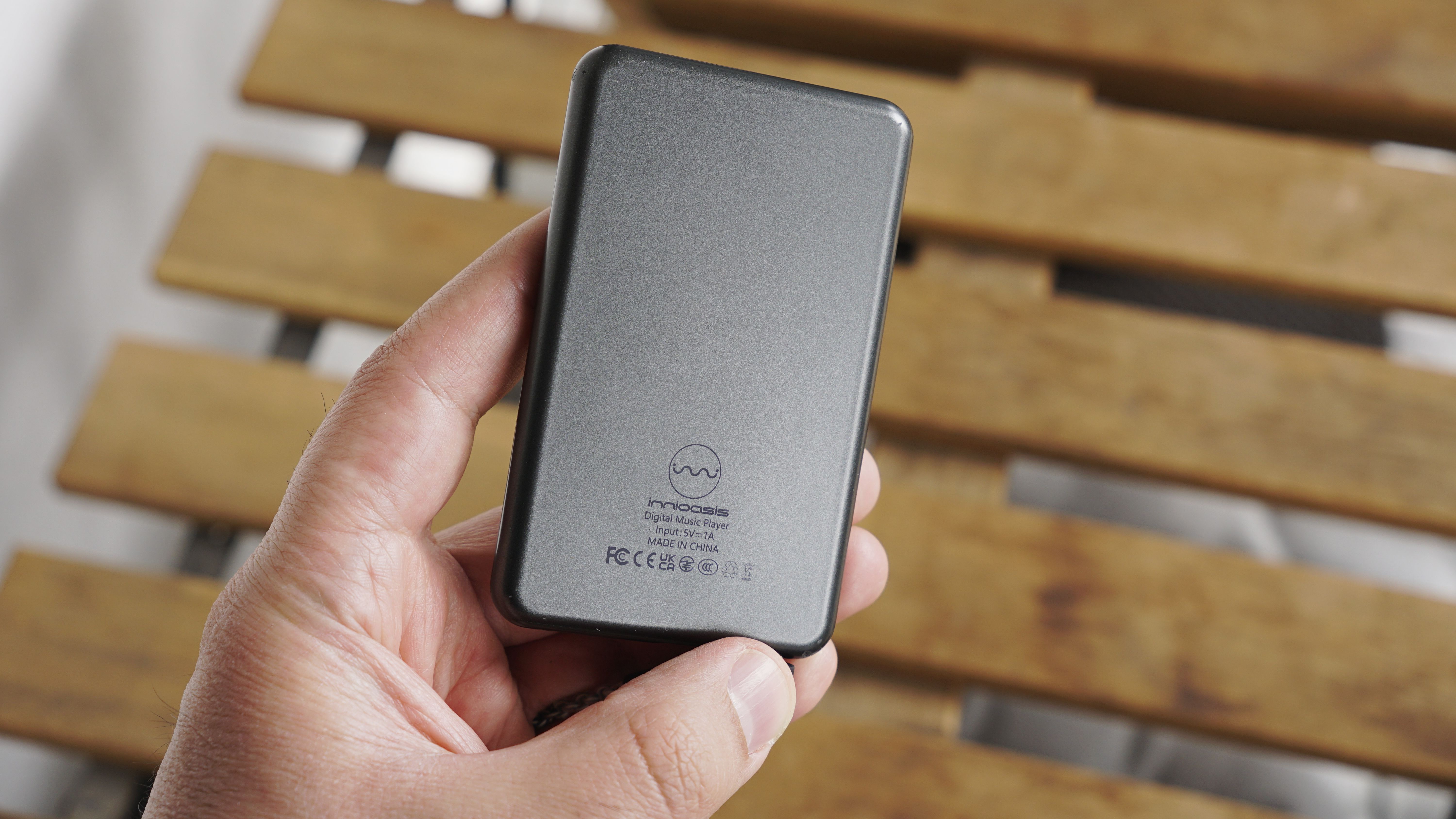 Innioasis Y1 player held in a man's hand, showing the dial and screen, with a wooden table in the background