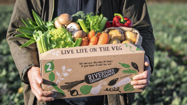 an image of one of the vegetable boxes from Riverford Organic being held by a farmer in a field