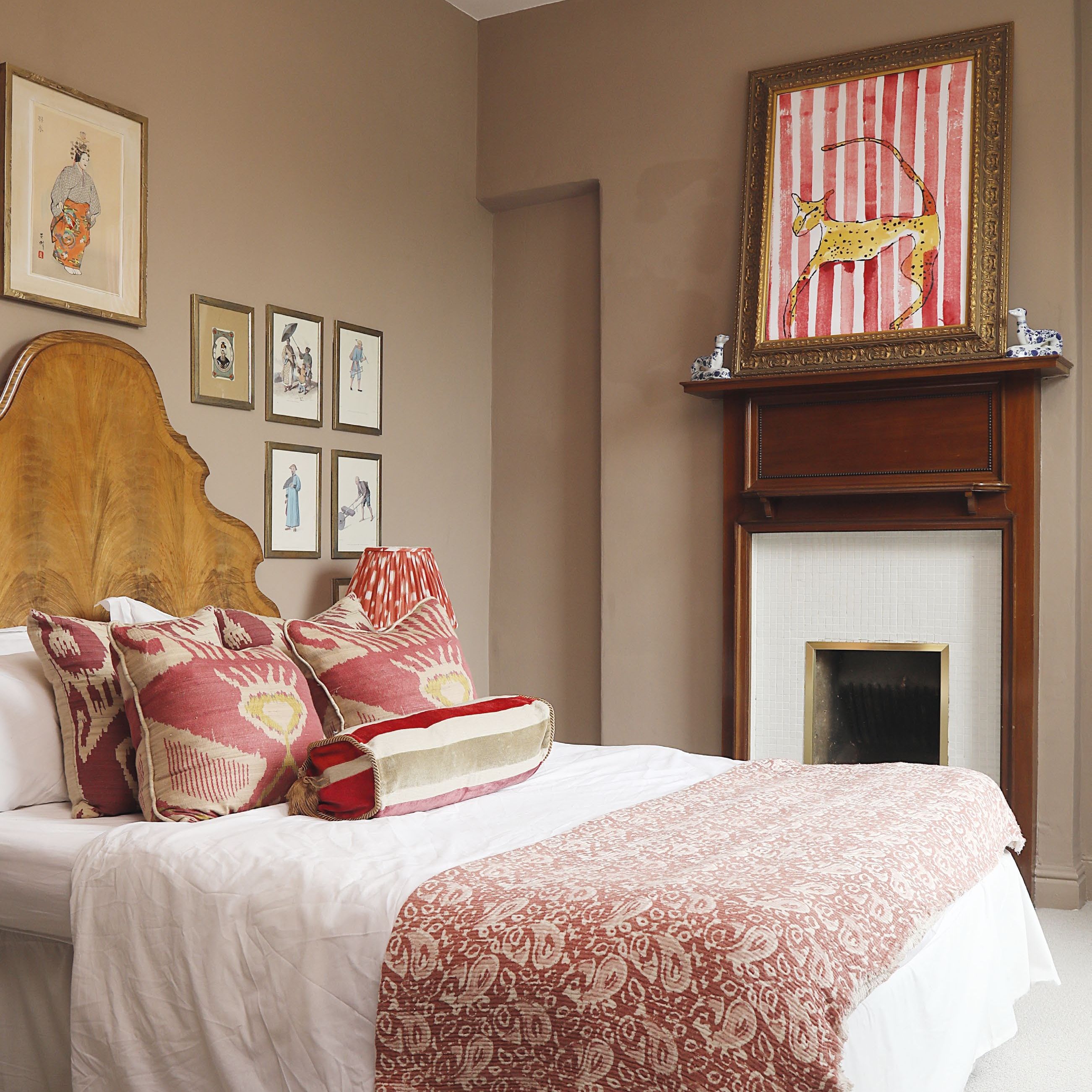 Classic style bedroom with stone coloured walls, antique wooden headboard and mix of scatter and bolster cushions