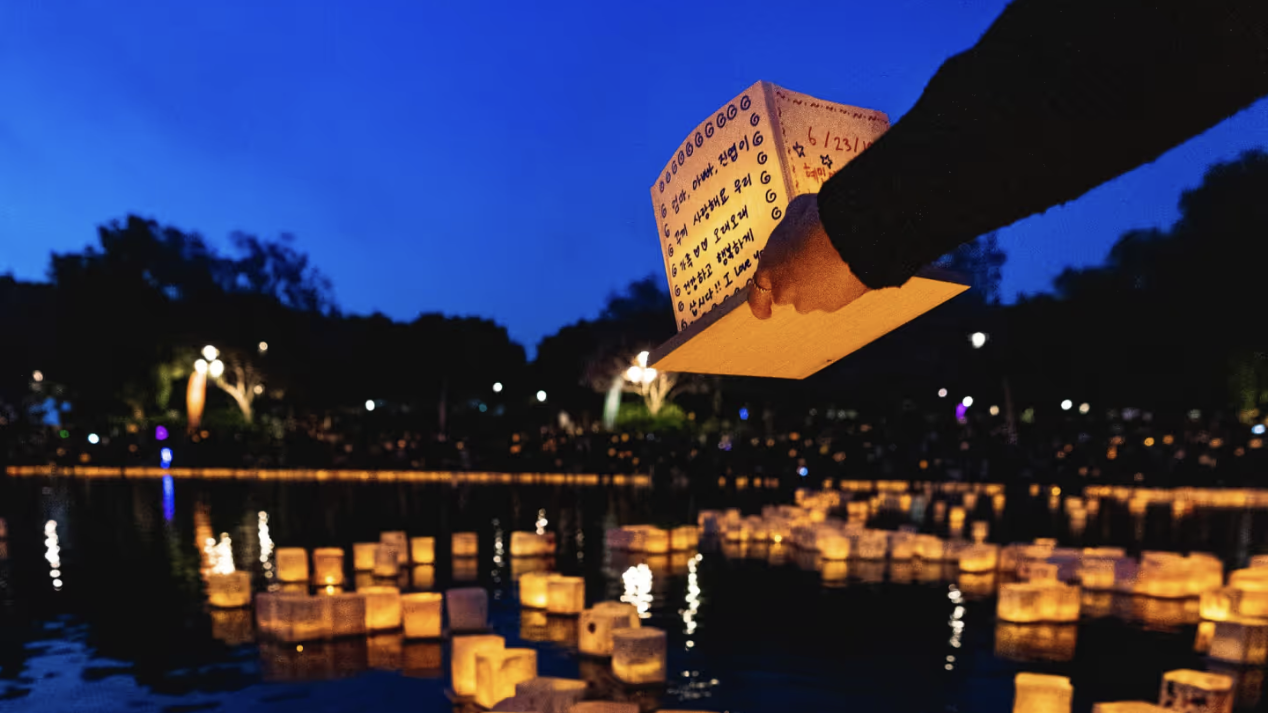 an image of someone reaching down to place a lantern on the lake, with a couple dozen other floating lanterns each with a written message on it
