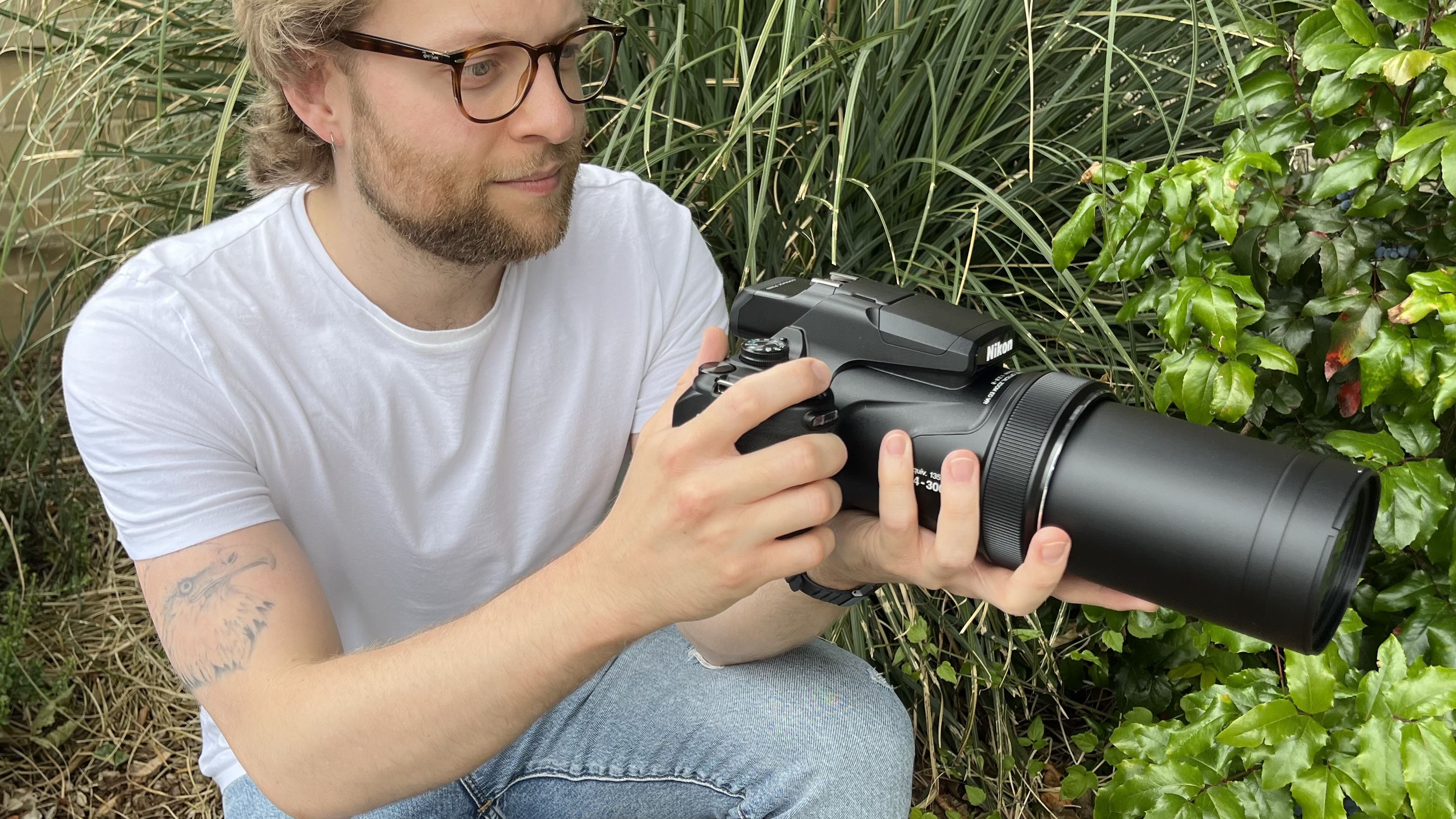 Nikon Coolpix P1100 lifestyle image of crouching Mike Harris holding P1100 in front of vegetation