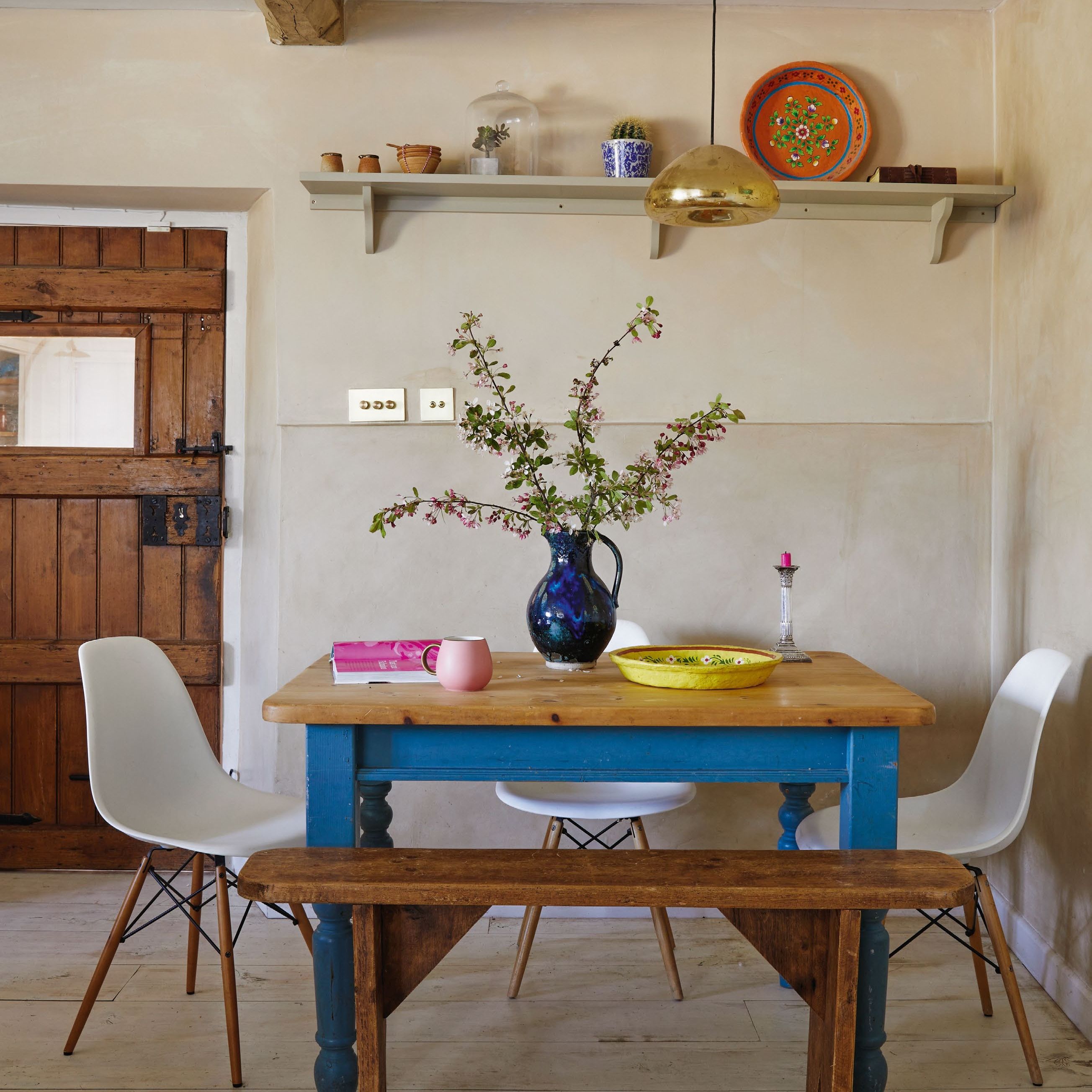 dining area in a kitchen with wooden table with blue painted legs, white Eames dining chairs and limewashed walls