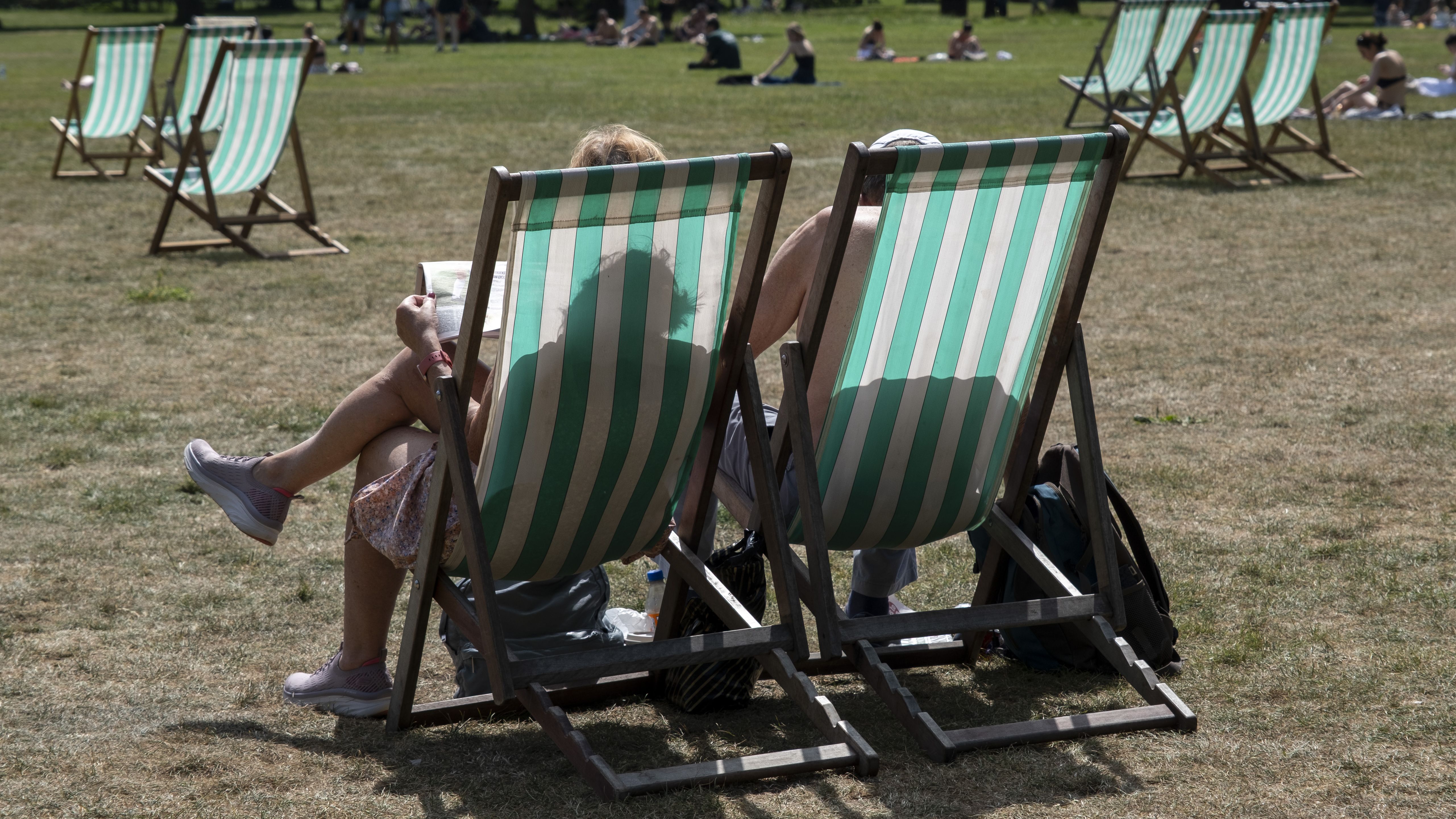 an image of a couple in Green Park using the rented deck chairs in the Spring heat during the start of the first heatwave of the year