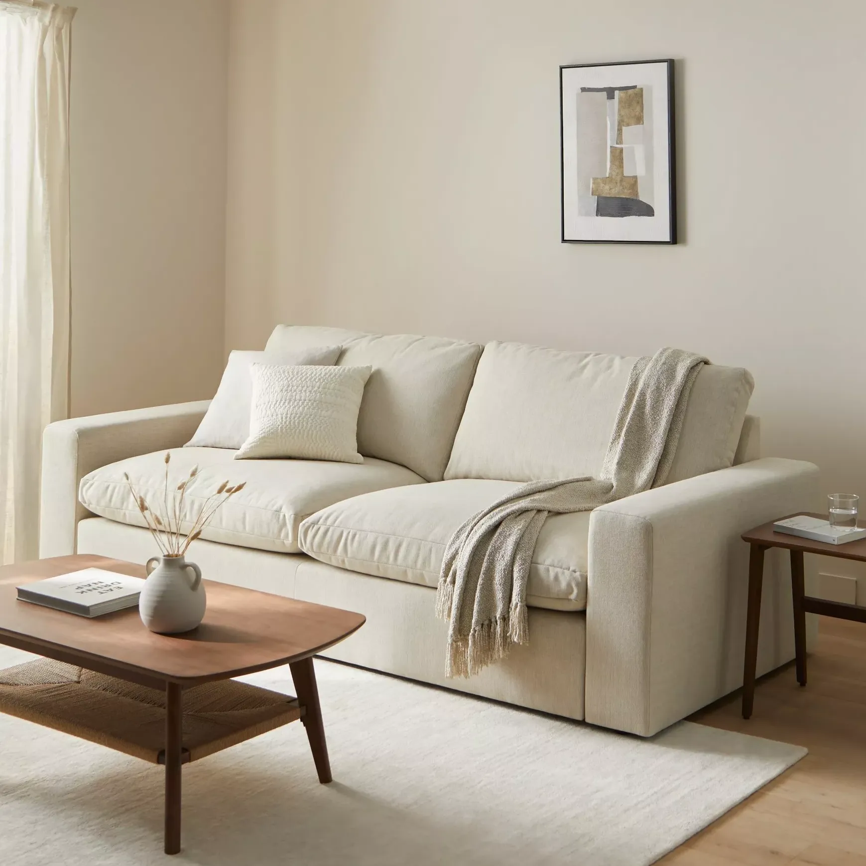 cream neutral sofa in a room with cream walls, small piece of neutral artwork on the wall and floor length linen curtains and wooden flooring