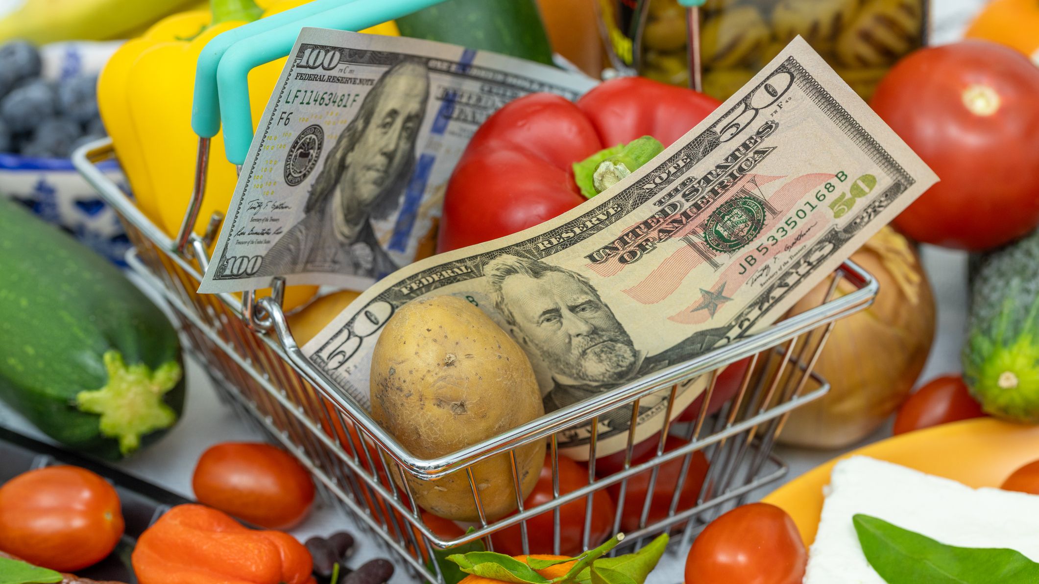 A basket of grocery items including tomatoes and zucchini with a $50 and $100 to signify inflation.