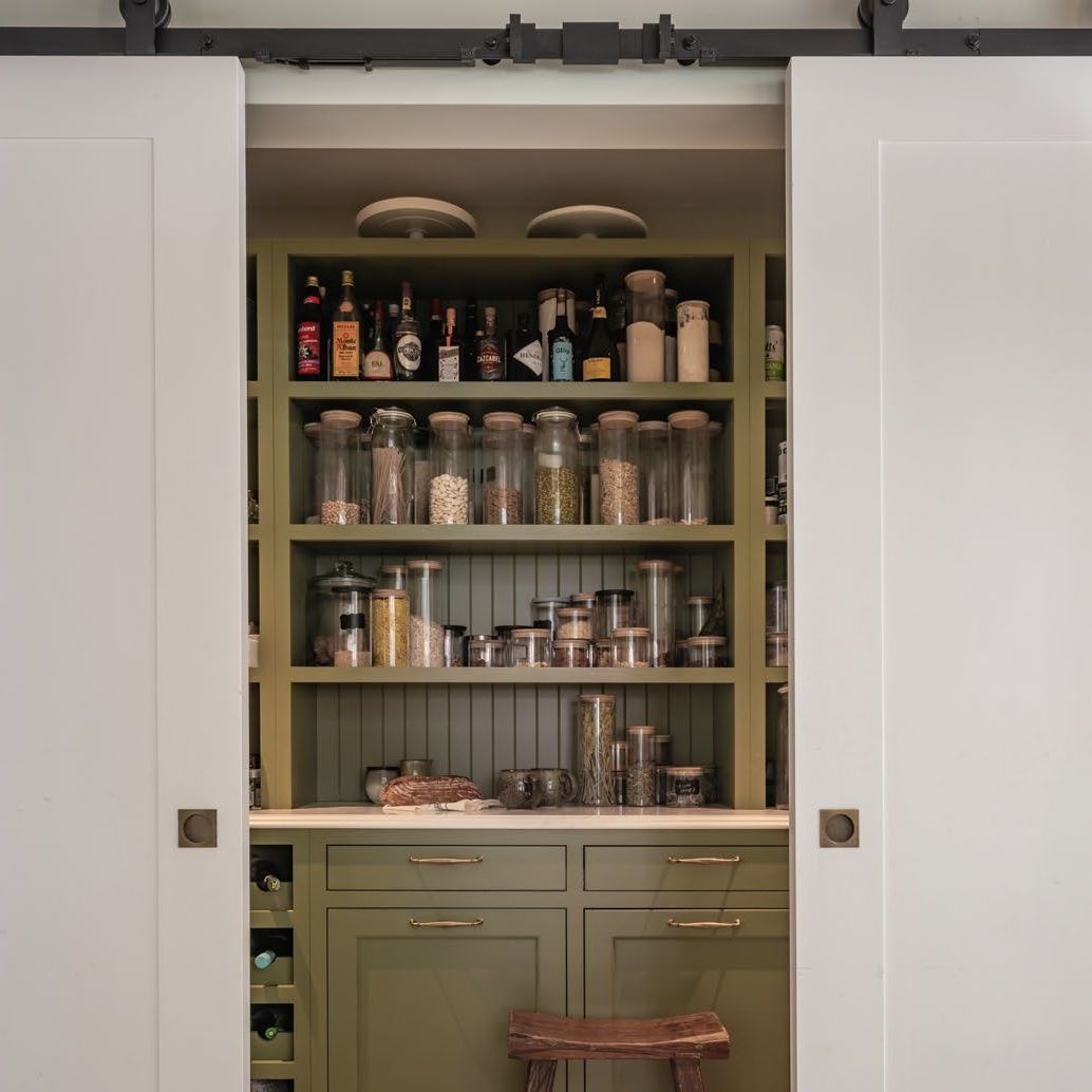 View into a pantry through sliding pocket doors with shelves and cupboards painted green