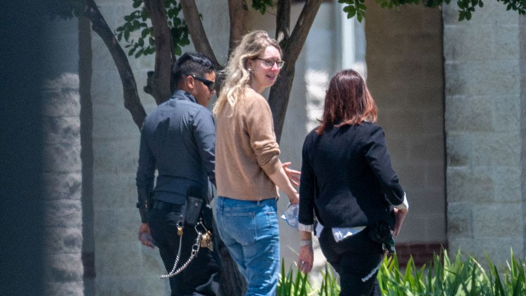 Elizabeth Holmes, wearing a brown sweater and jeans, walks into a federal prison camp.