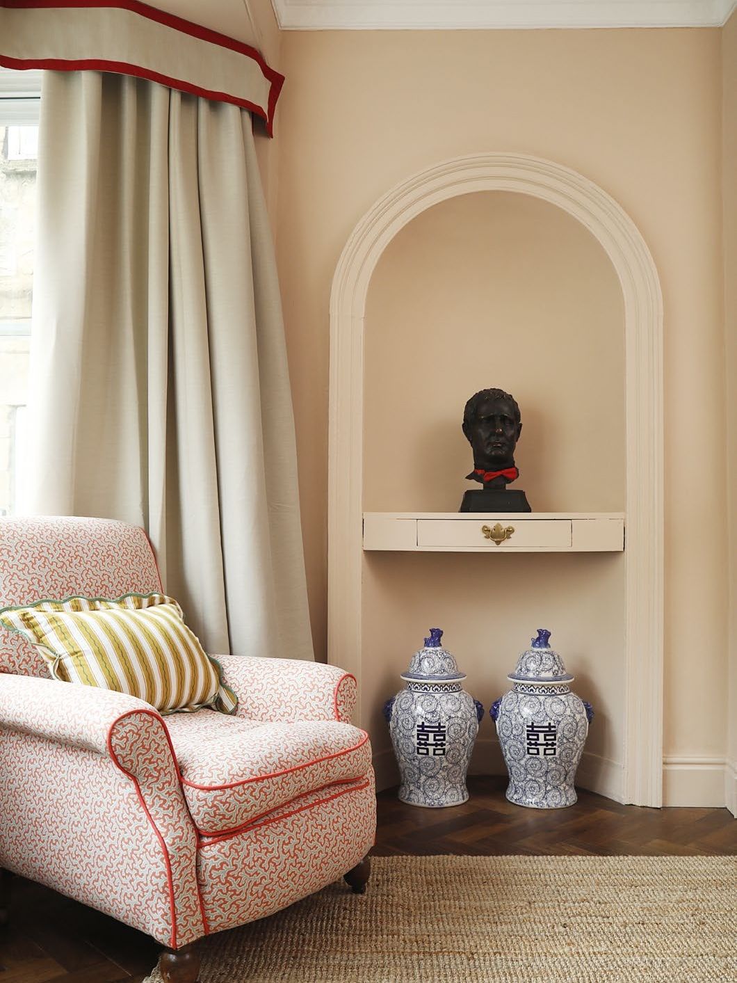 Traditional armchair with cushion beside an arched alcove with bust on shelf and ceramic urns on floor