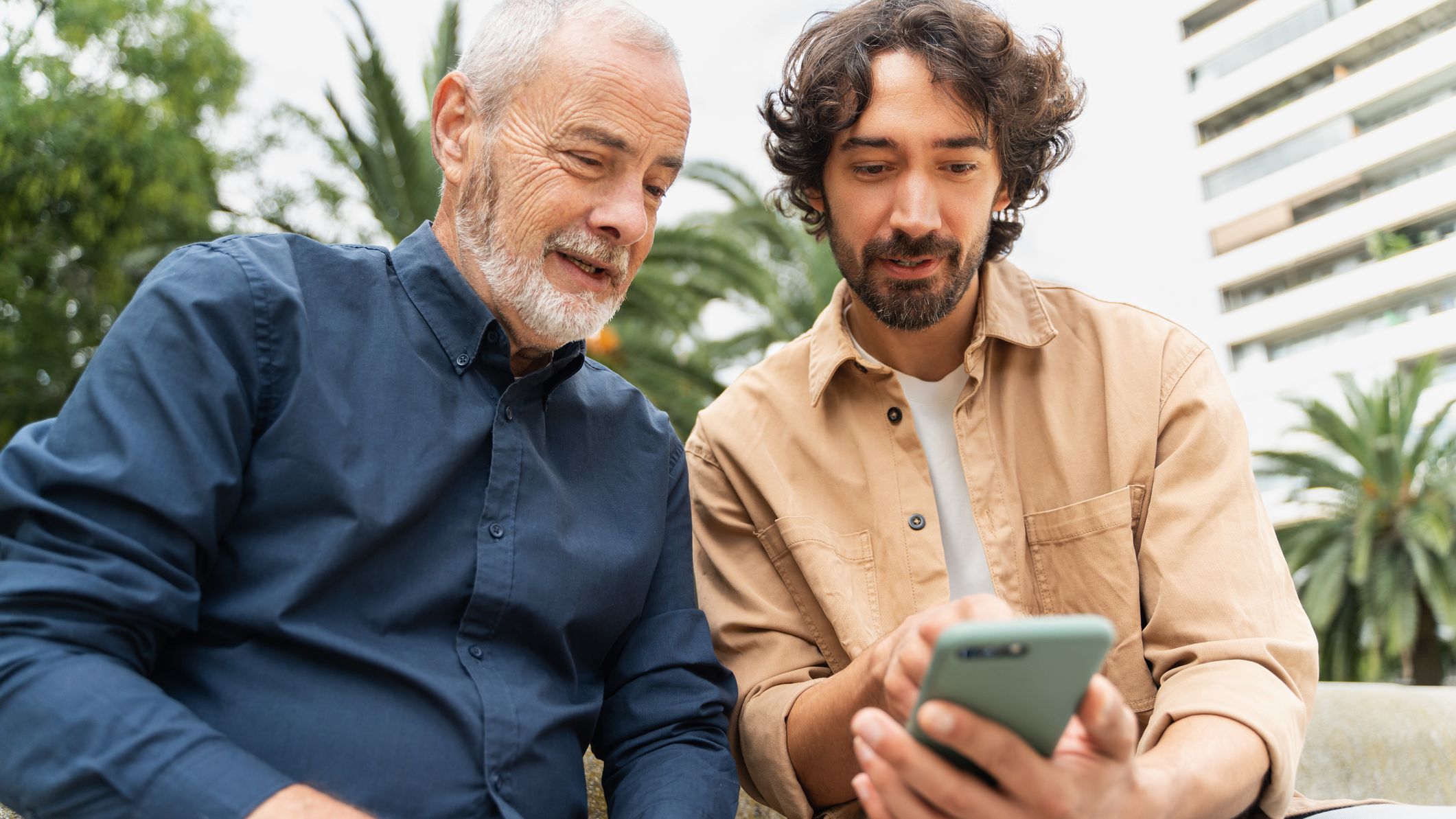 Father and adult son look at a phone.