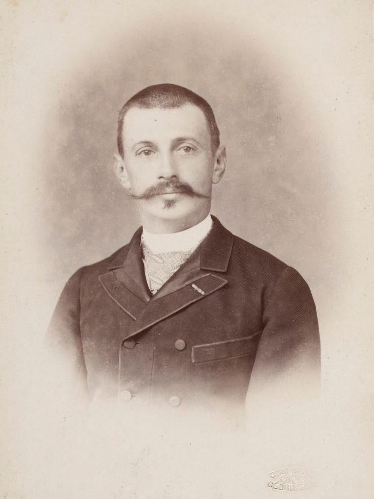 A brown photograph of a moustached man looking at the camera