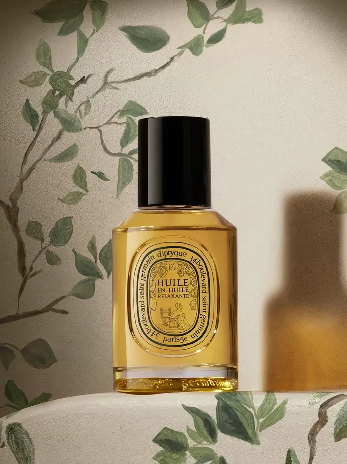 A product shot of the Diptyque Relaxing oil-in-oil, in front of a painted green leaf background
