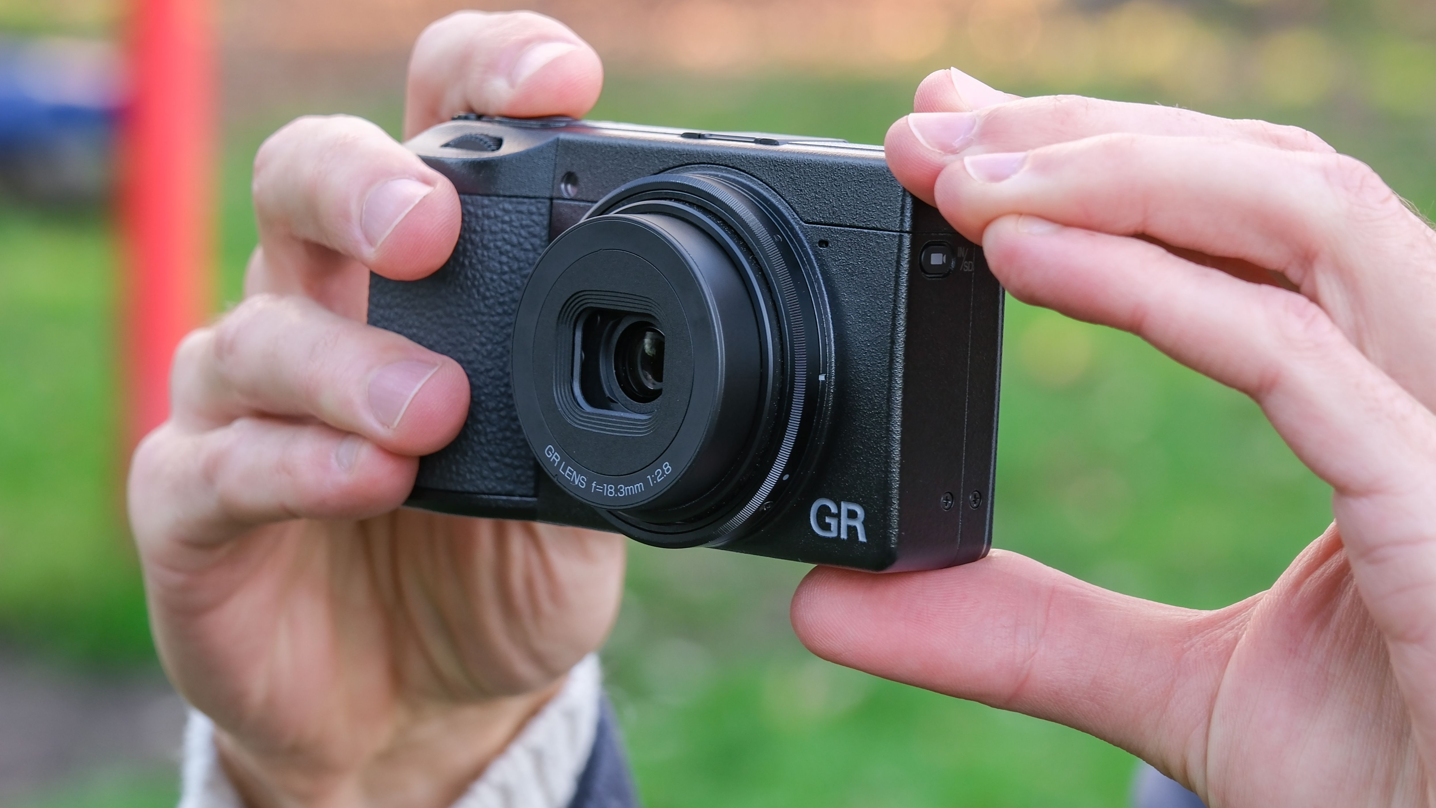 Ricoh GR IV compact camera held in a pair of hands