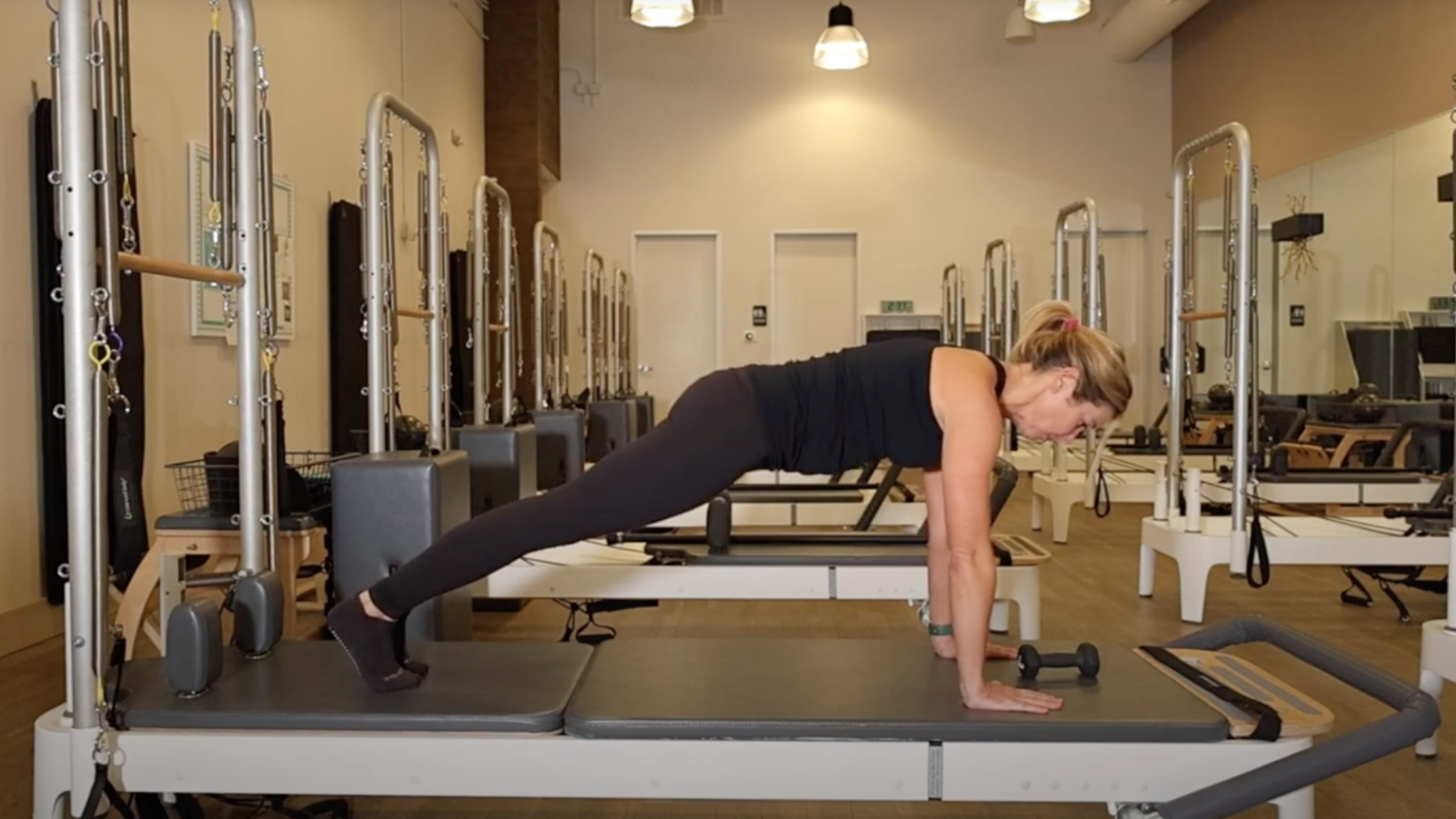 Woman demonstrates plank position on a Reformer bed in a Pilates studio