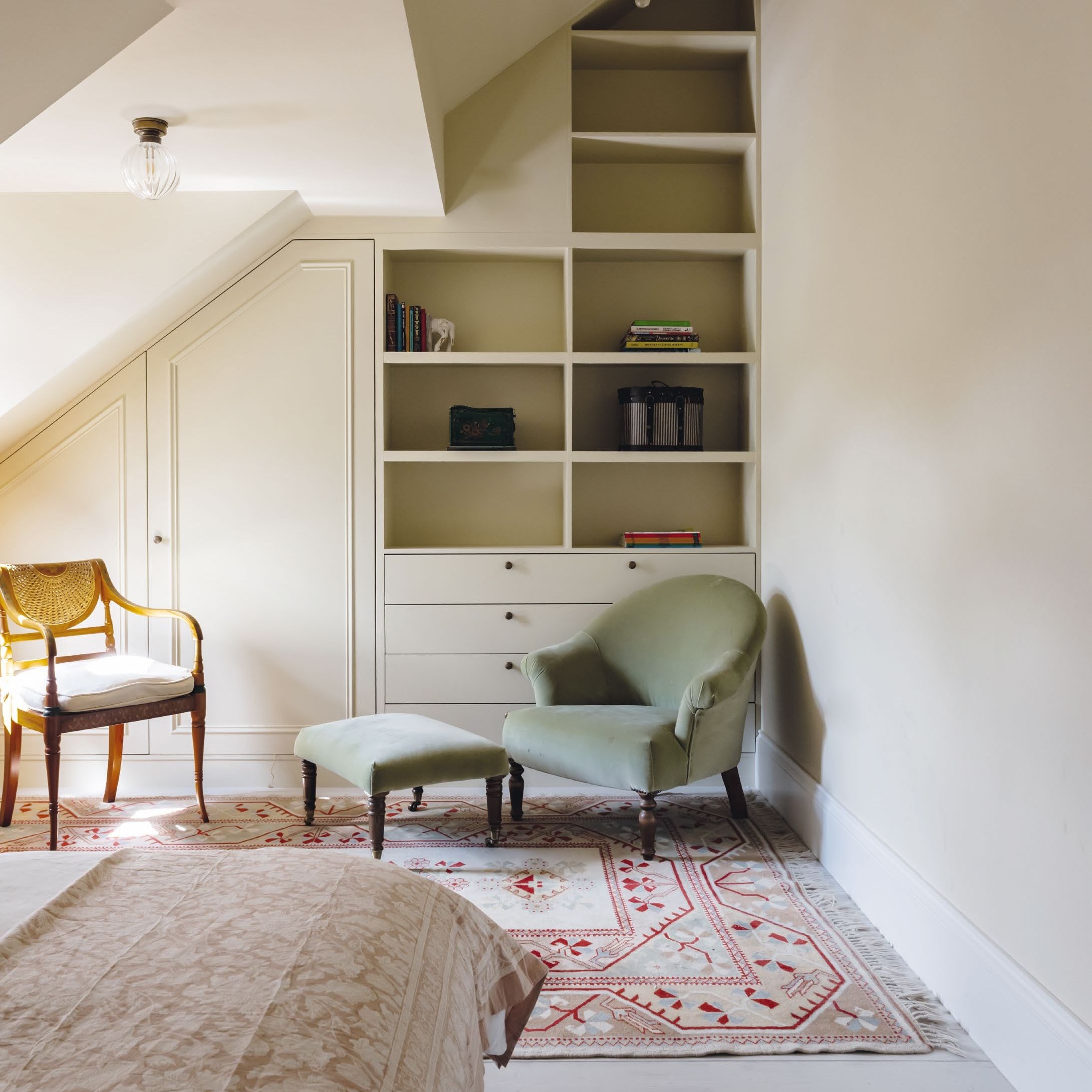 Attic bedroom with fitted cupboard and shelving and small armchair and footstool