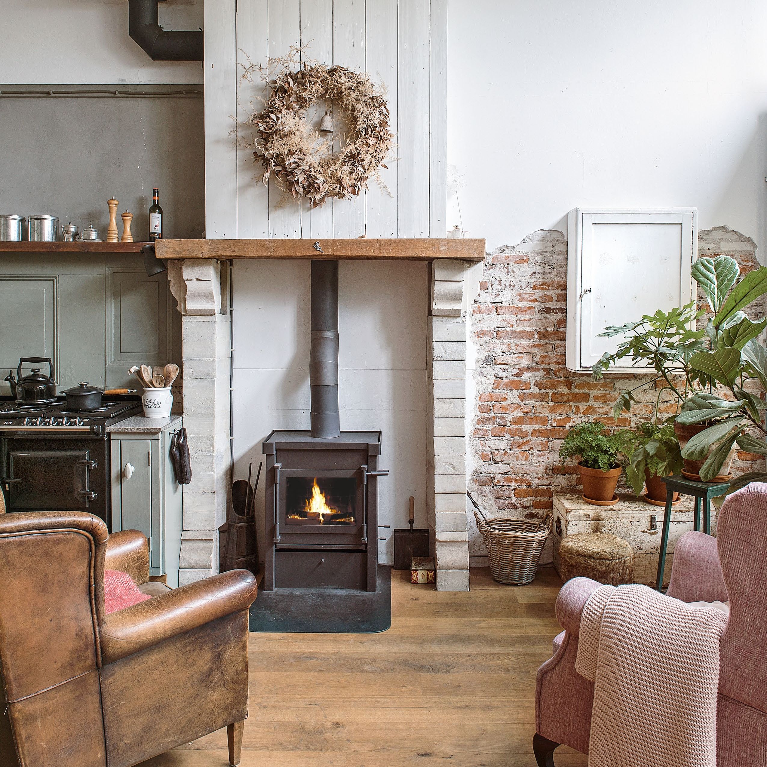 View towards a wood burner with two armchairs in front, in an open-plan kitchen living space