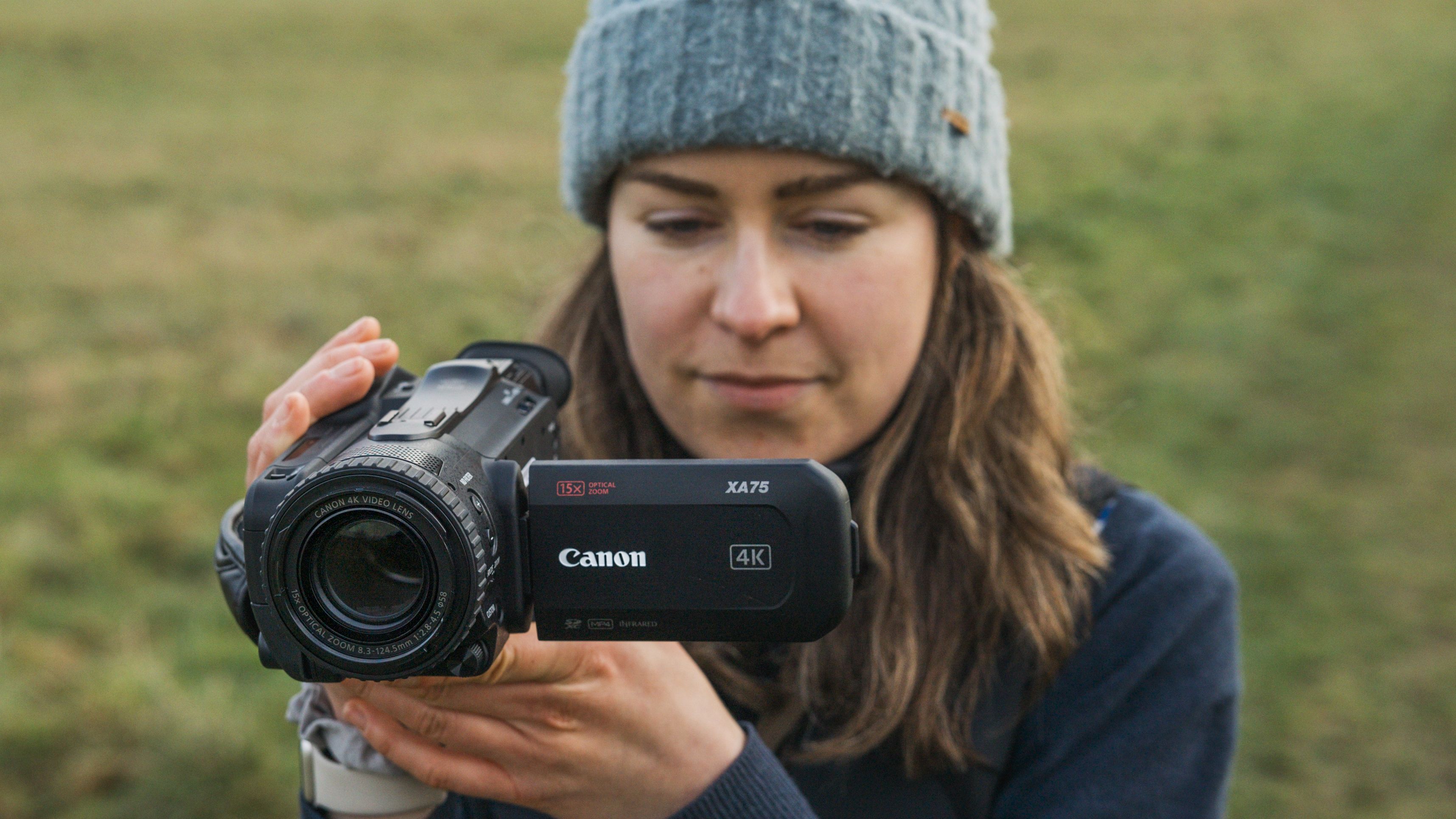 The Canon XA75 camcorder held by a woman in a hat on a field