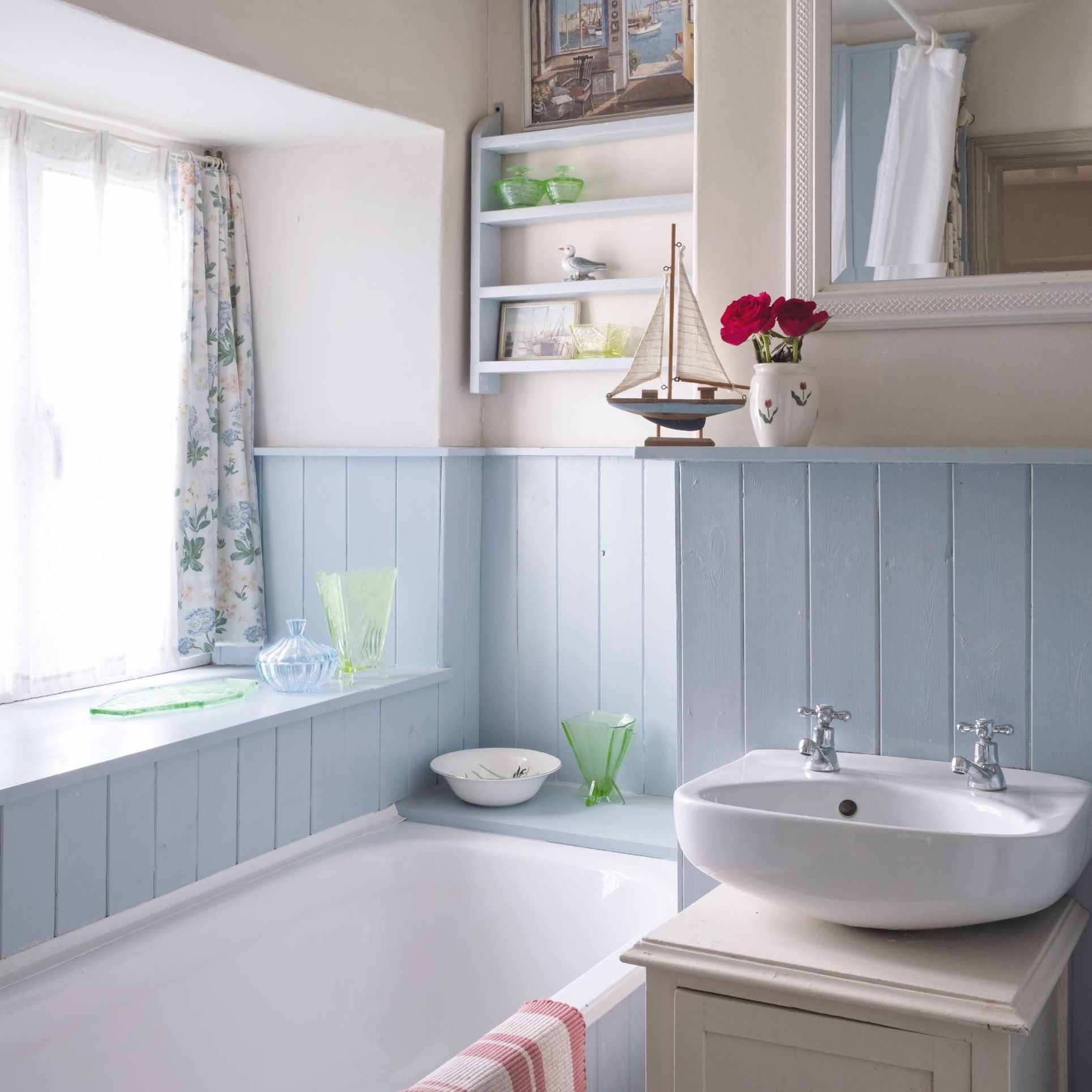Small cottage bathroom with blue painted tongue and groove panelling and floral curtains